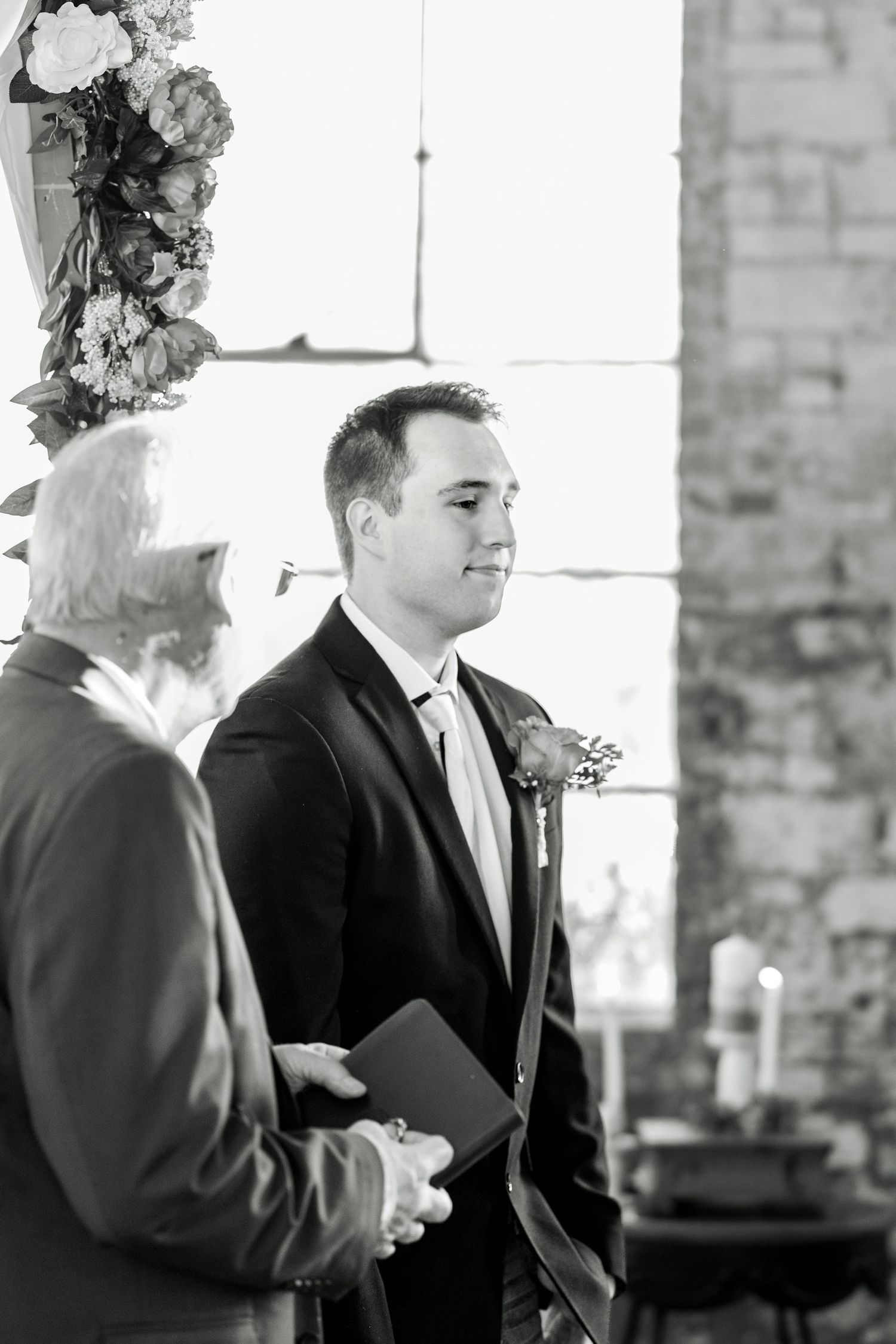 Black and white ceremony photo showing officiant and groom at wedding altar.