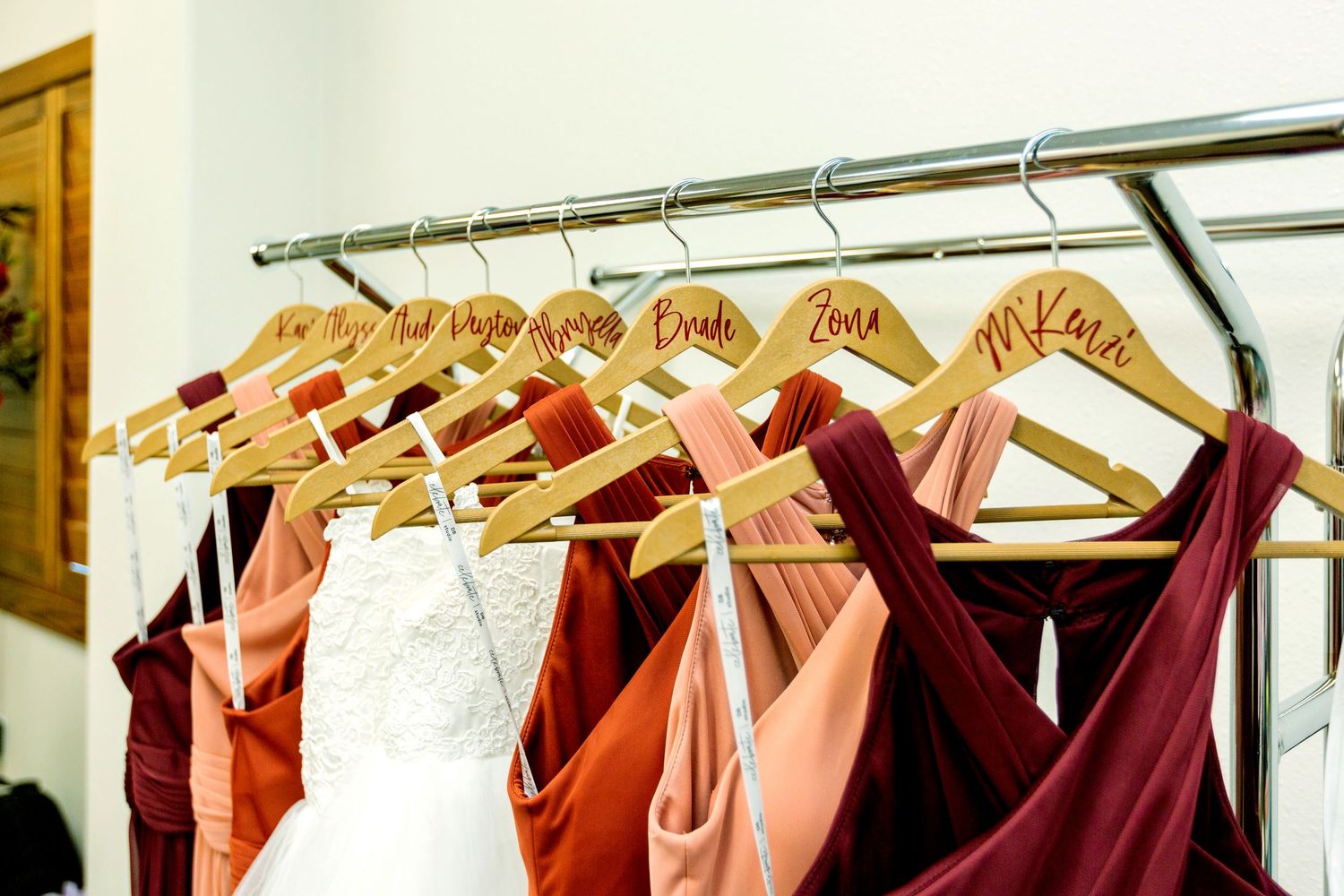 Row of colorful bridesmaid dresses hanging on wooden hangers in a boutique.