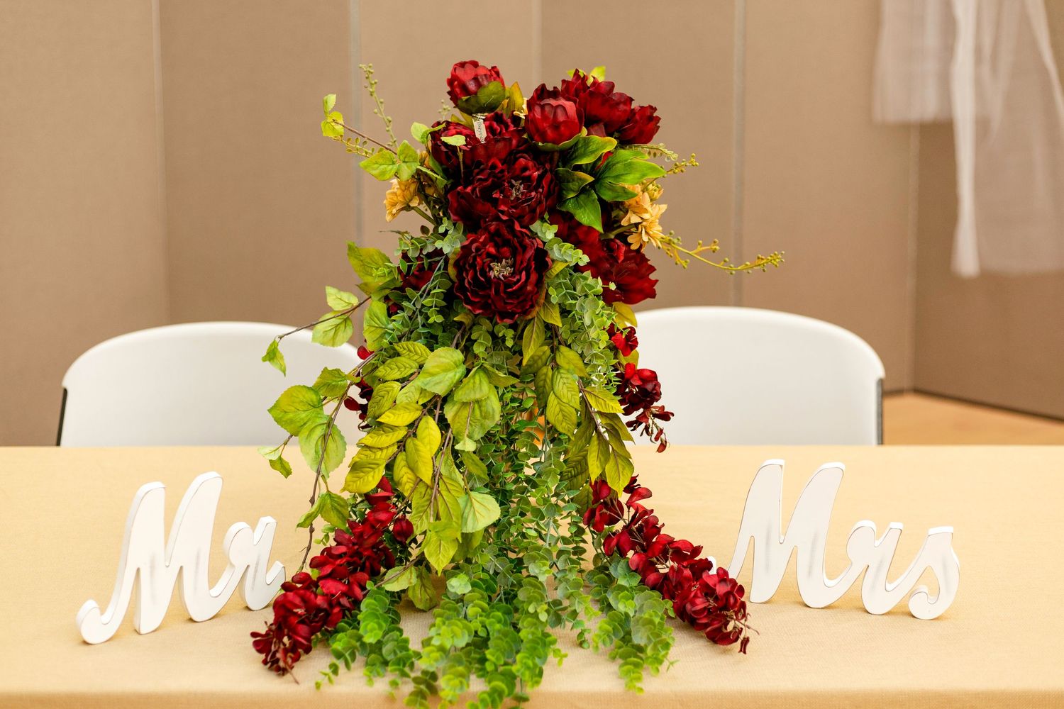 Elegant floral arrangement with deep red blooms and cascading greenery on a white background.