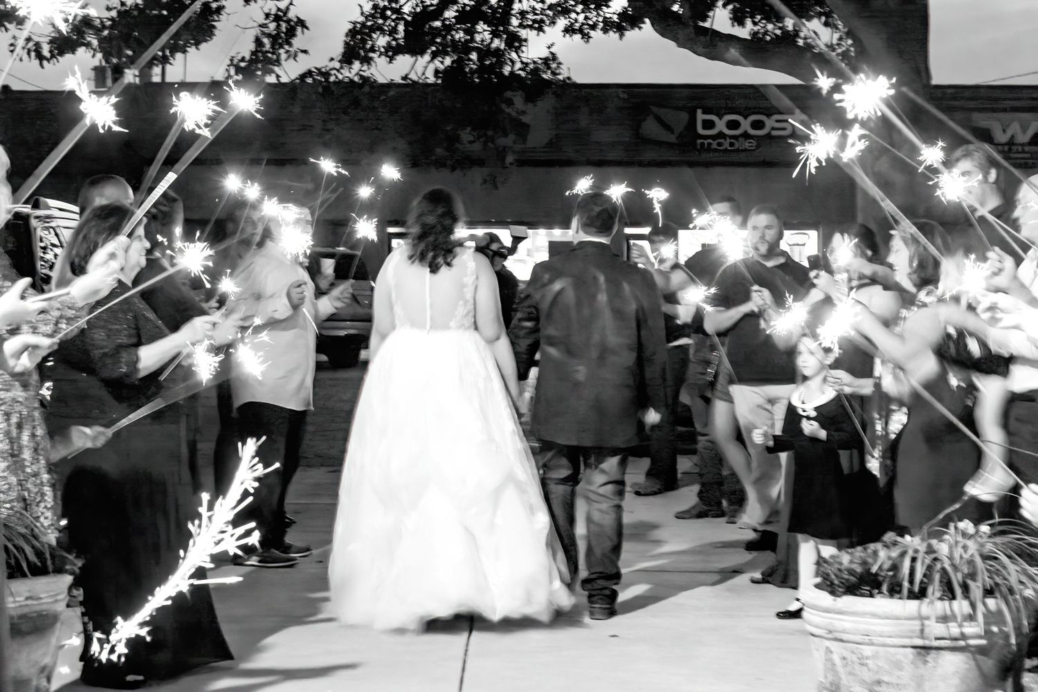 Wedding couple exits venue under glowing sparklers held by guests during nighttime celebration.