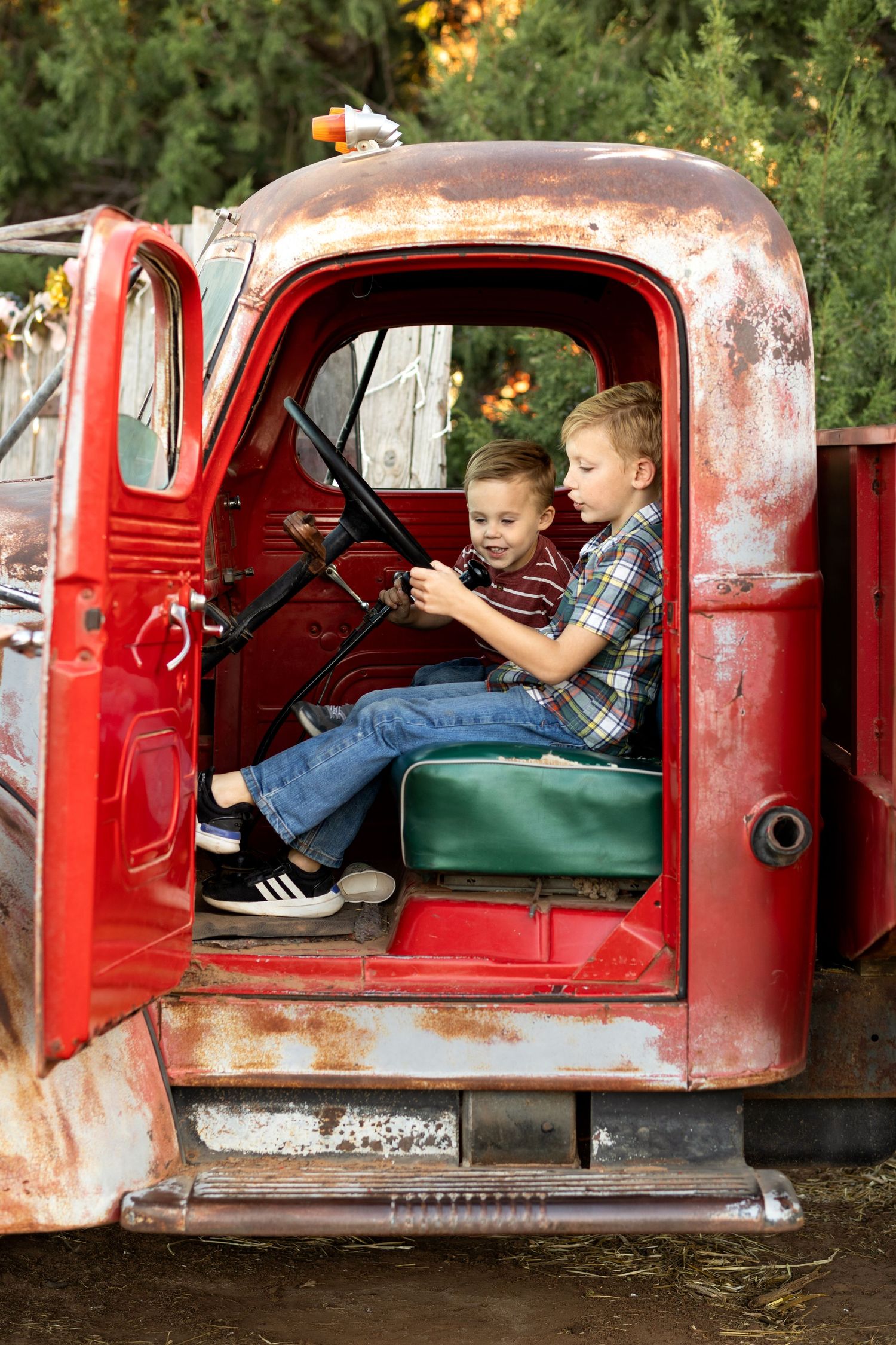 Children playing inside a vintage red truck during a rustic outdoor photo session.