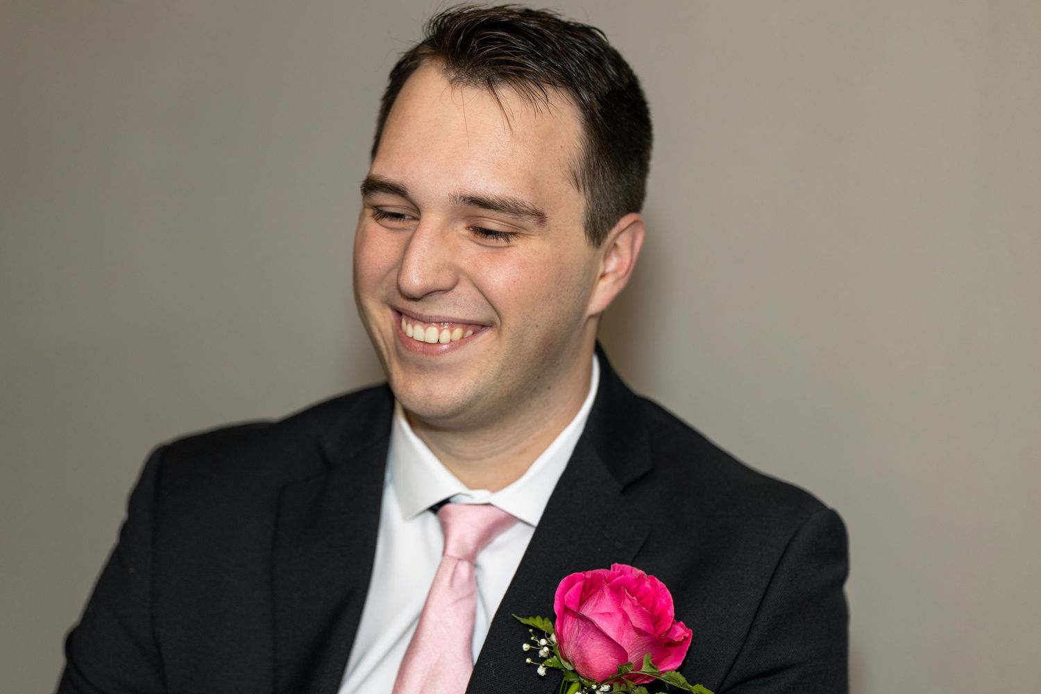 Wedding portrait showing boutonniere with pink rose against dark suit.