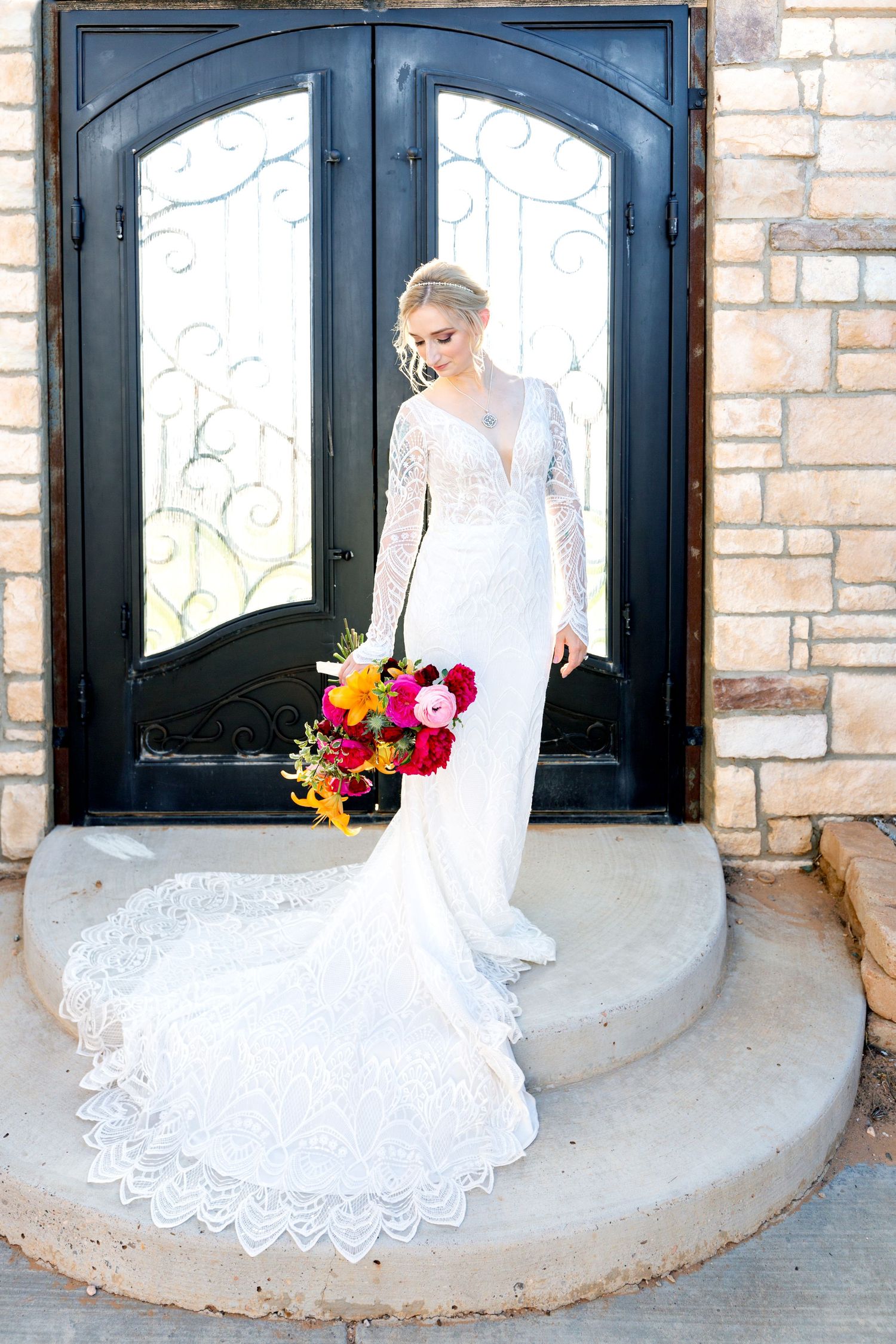 A beautiful lace wedding dress with a flowing train displayed against a stone wall backdrop.