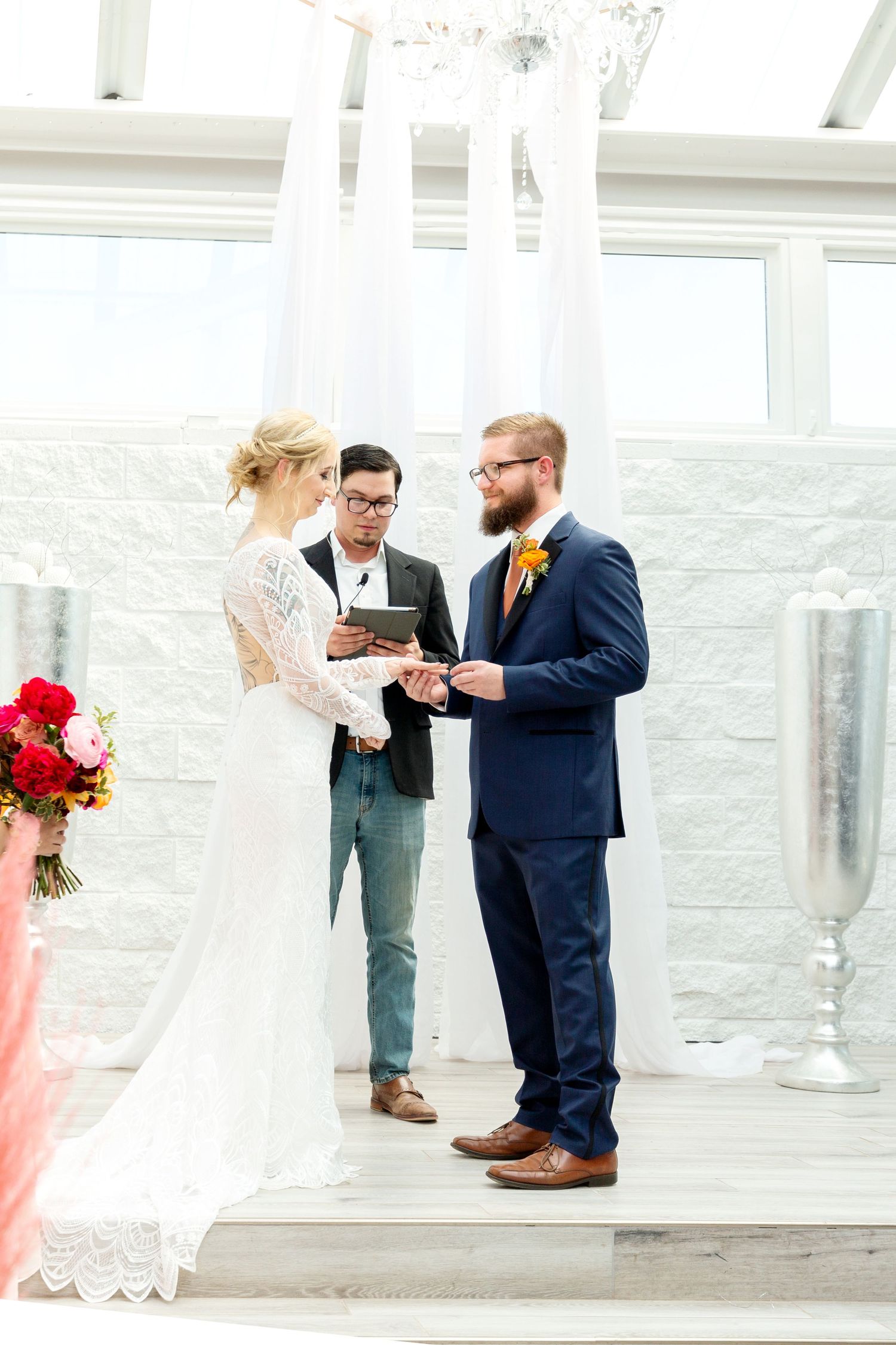 Wedding ceremony in bright white venue with couple exchanging vows at the altar.