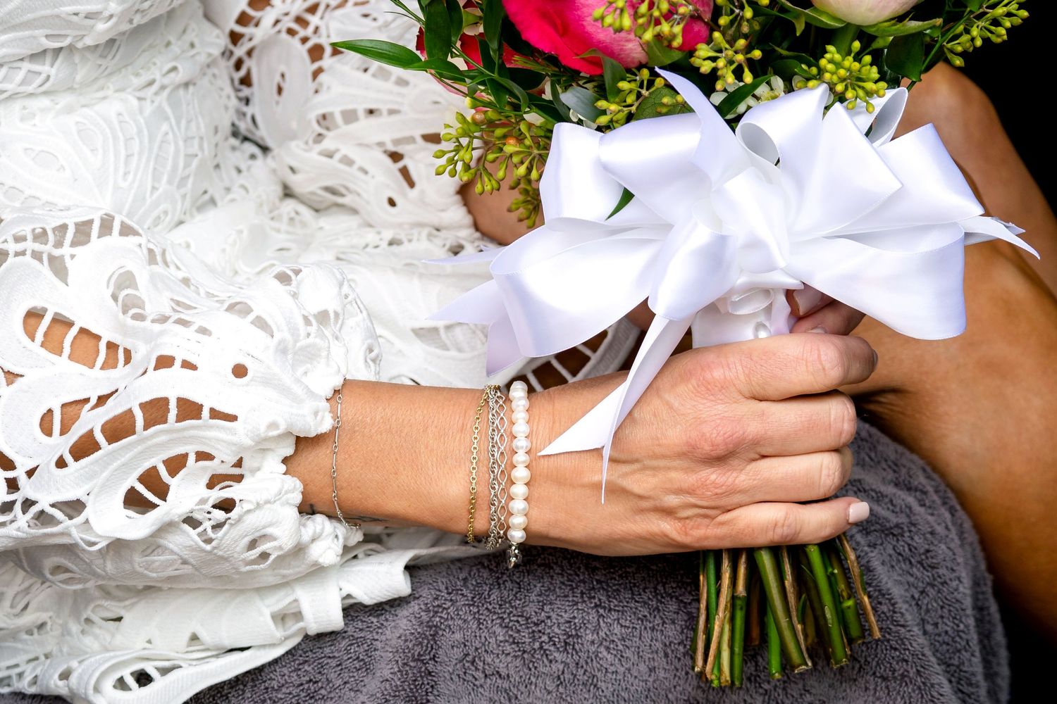 Close-up details of a white lace wedding dress and bridal bouquet with red flowers.