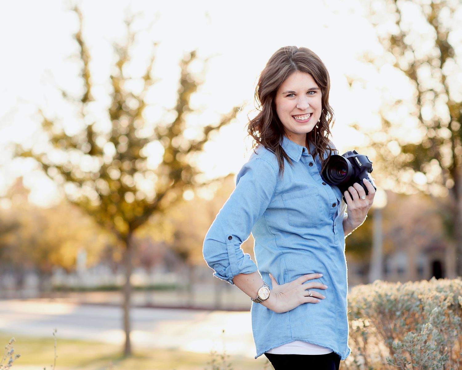 Woman in light blue shirt posing outdoors during golden hour sunset.