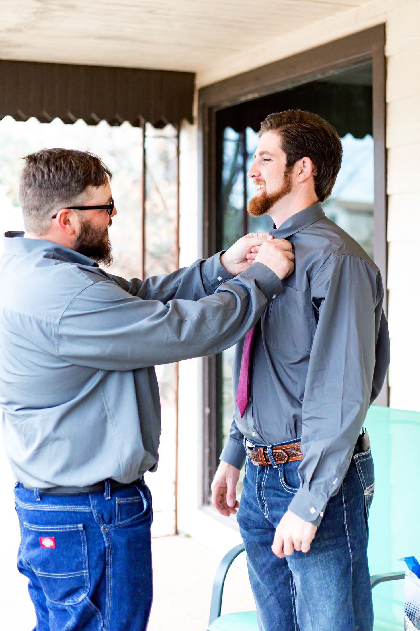 Two people in casual attire adjusting tie and formal wear before event.