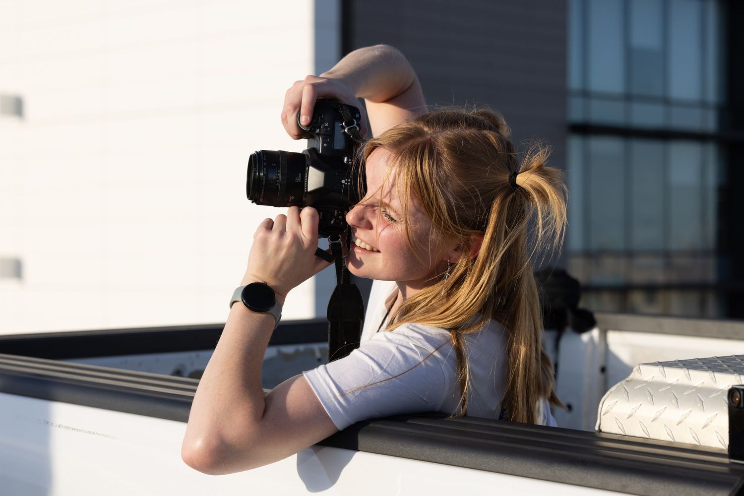 Female photographer taking pictures while leaning out of car window with professional camera.
