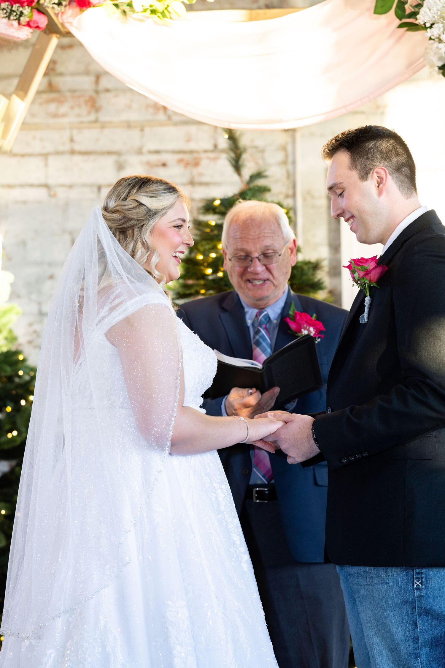 Exchange of rings ceremony during indoor wedding with Christmas lights in background.