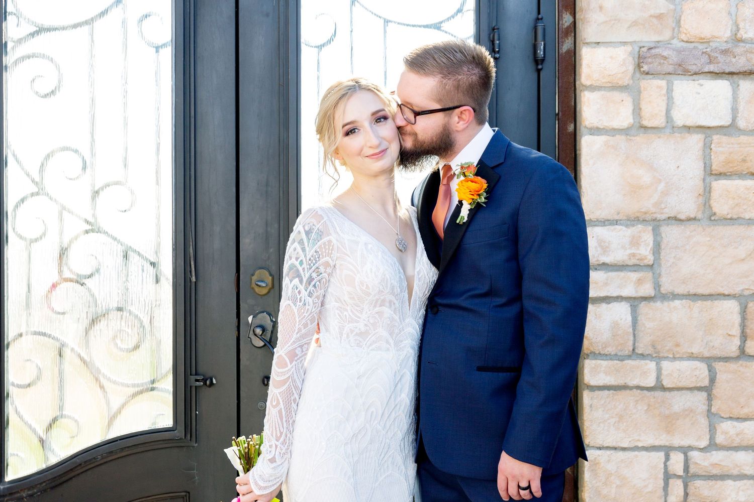 Couple sharing romantic moment outside stone building with ornate iron door.