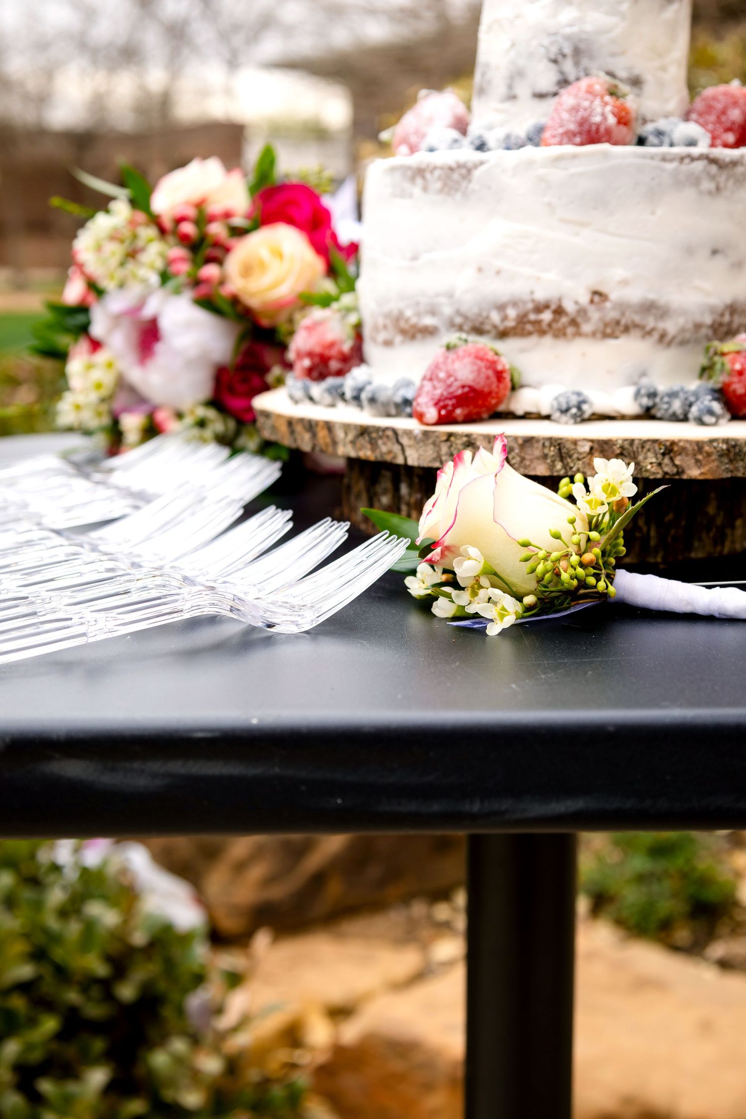 Wedding cake display with fresh flowers on rustic wood slices against black tablecloth.