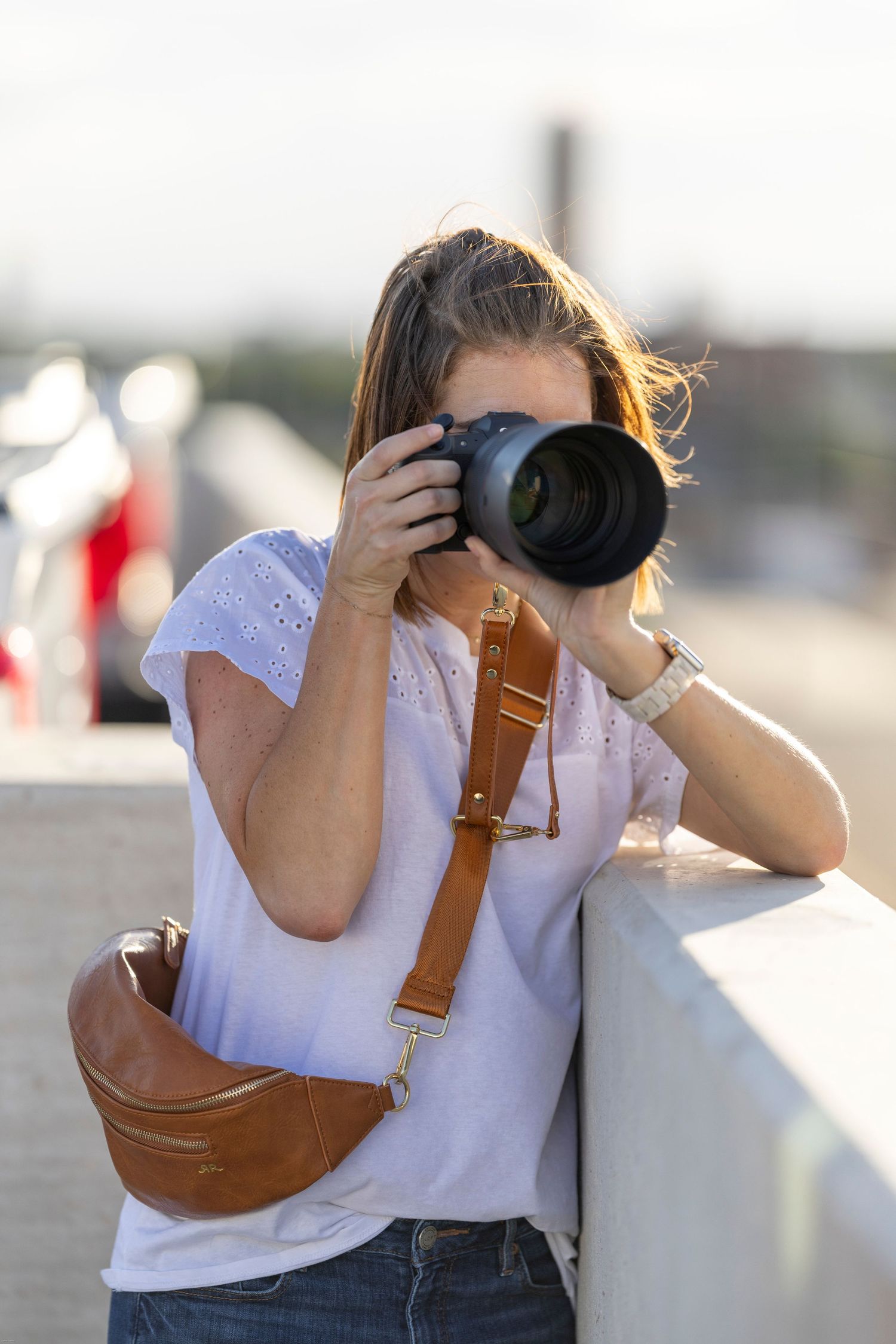 Photographer wearing white shirt and brown camera strap taking photos outdoors.
