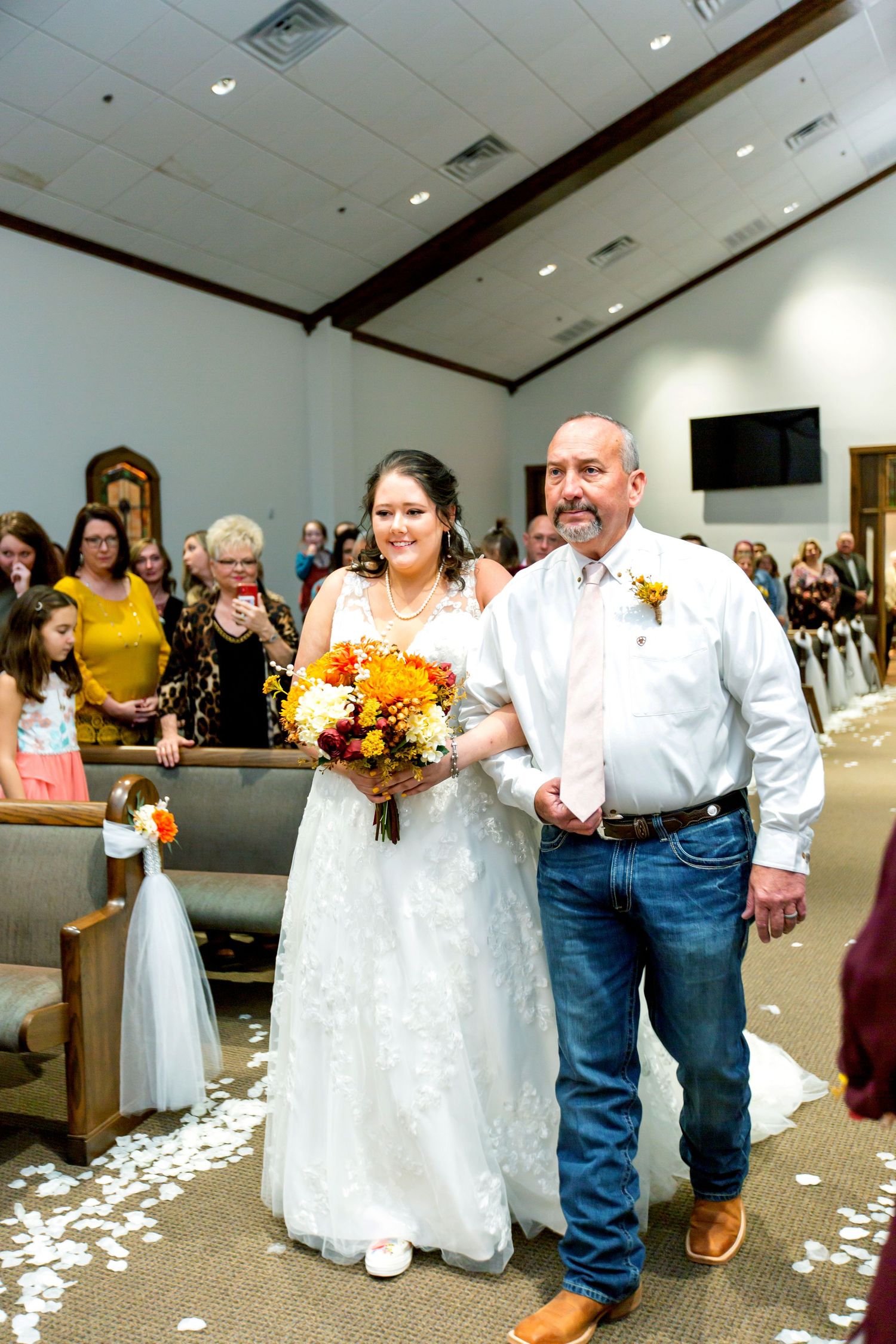Wedding ceremony procession in a church with white petals scattered along the aisle.