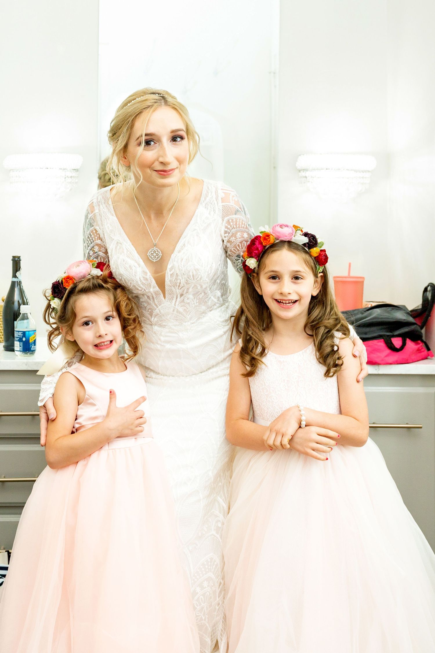 Young flower girls in pink tulle dresses pose with bride in white lace gown.