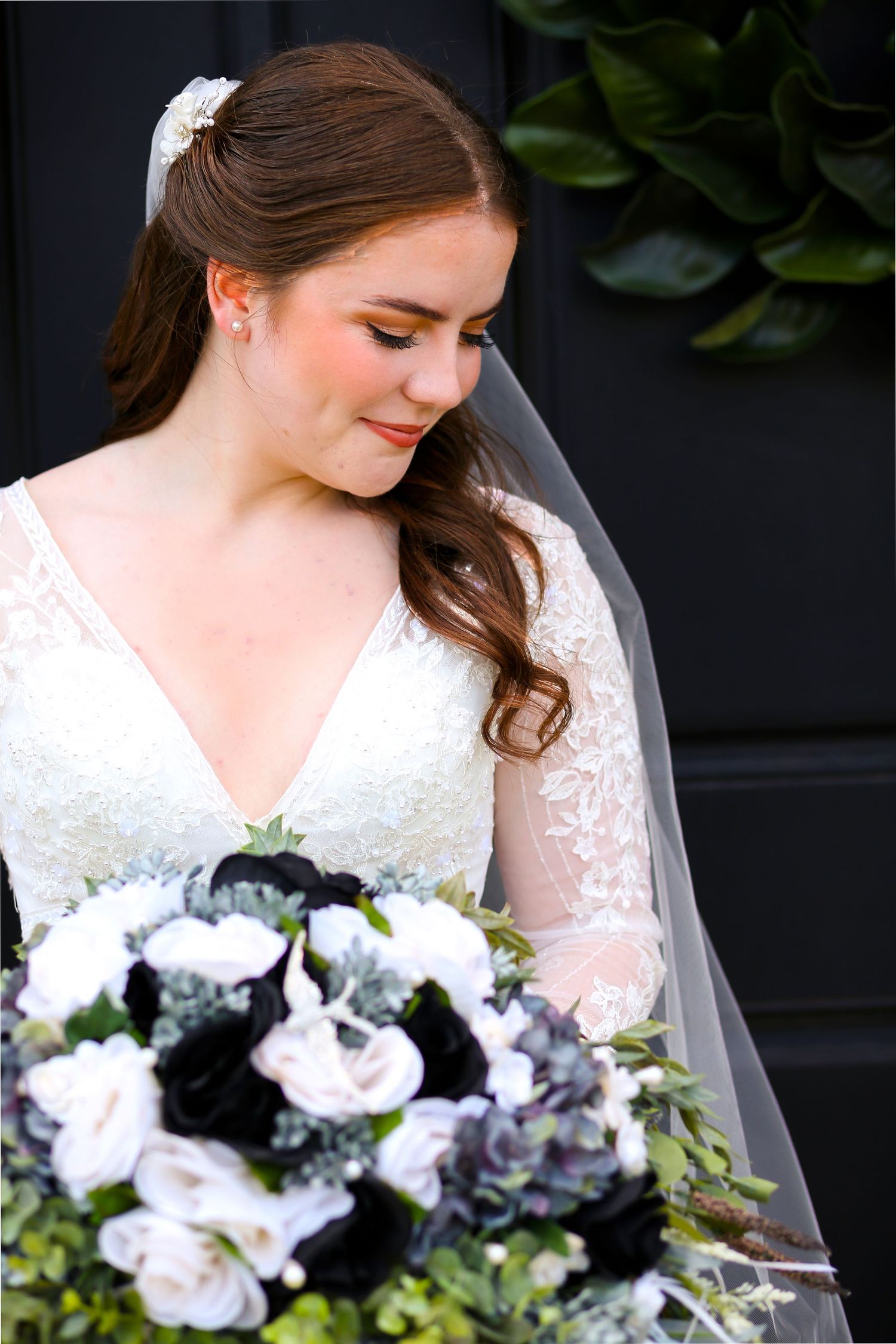 A bridal portrait showcasing a lace wedding gown and bouquet with navy and white flowers.