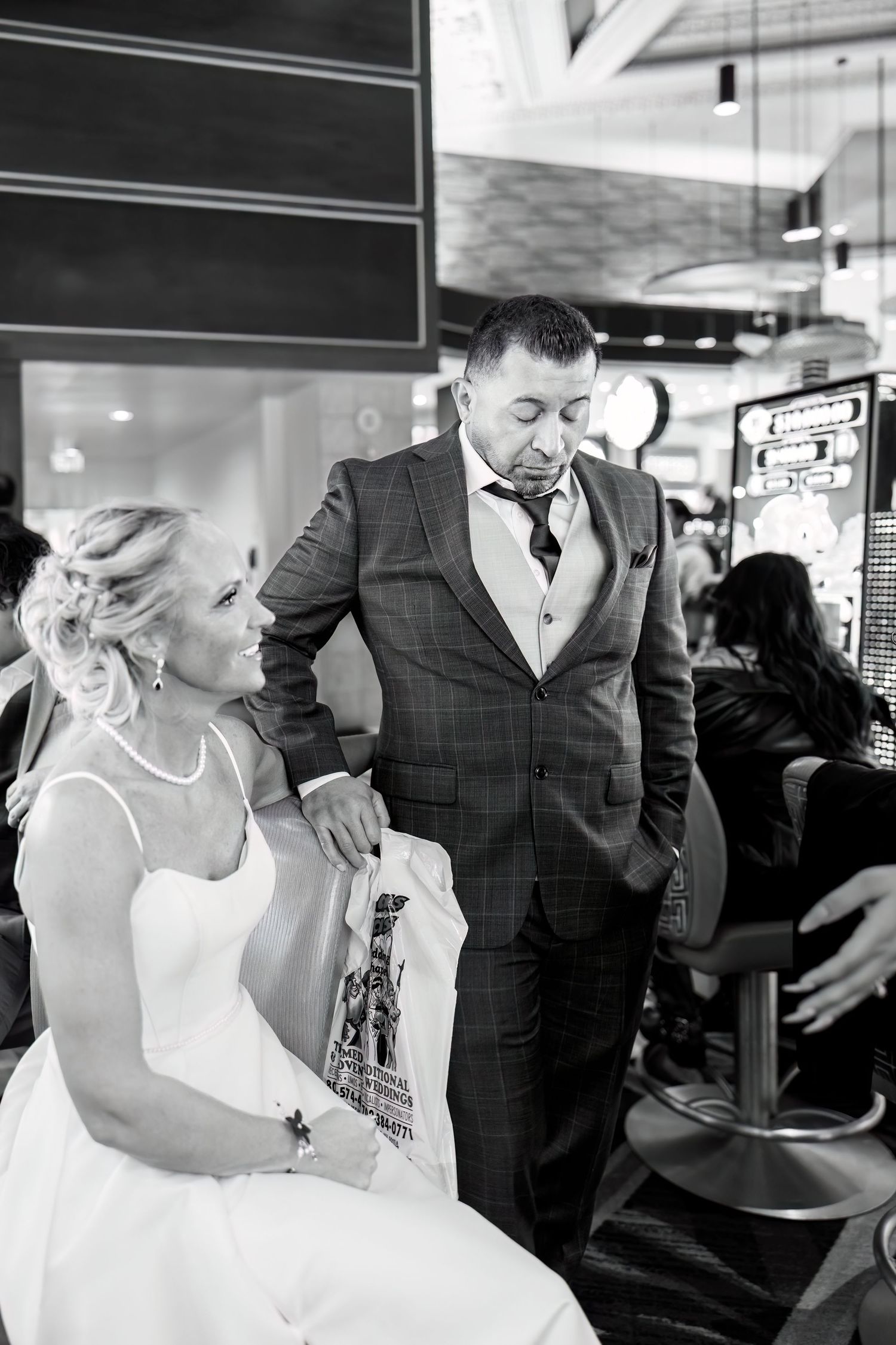 A candid black and white moment at a wedding reception showing a couple in formal attire.
