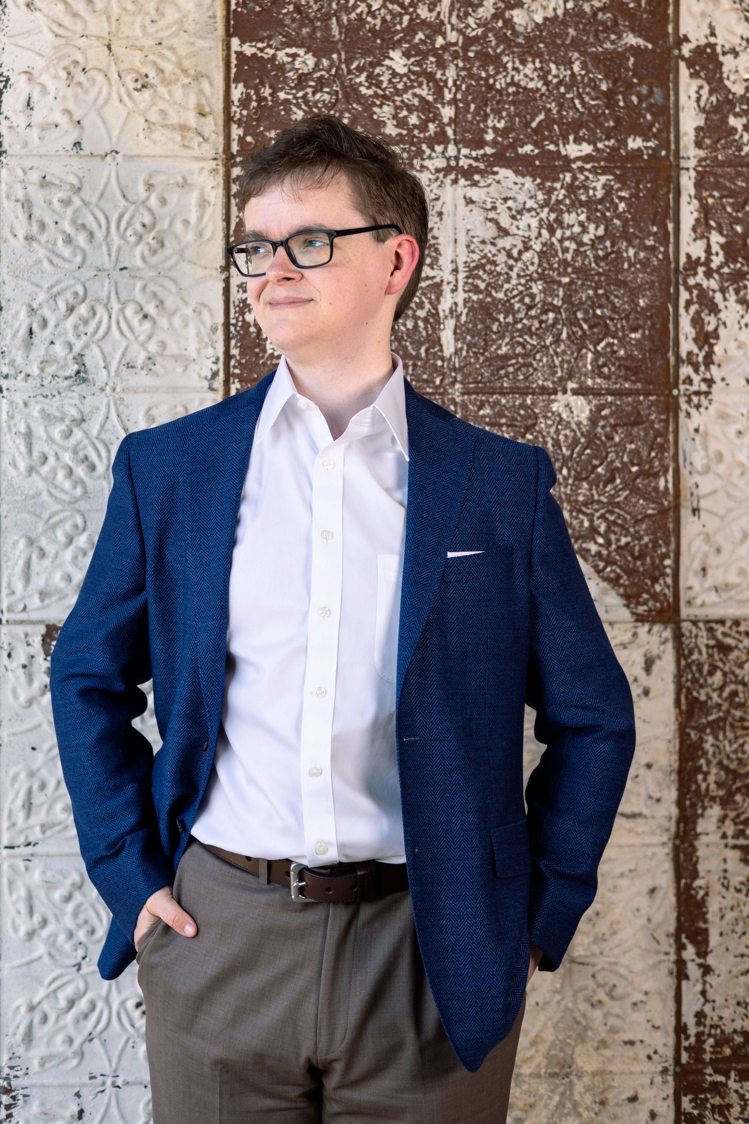 Person in navy blazer and white shirt poses against textured wall during professional photoshoot.