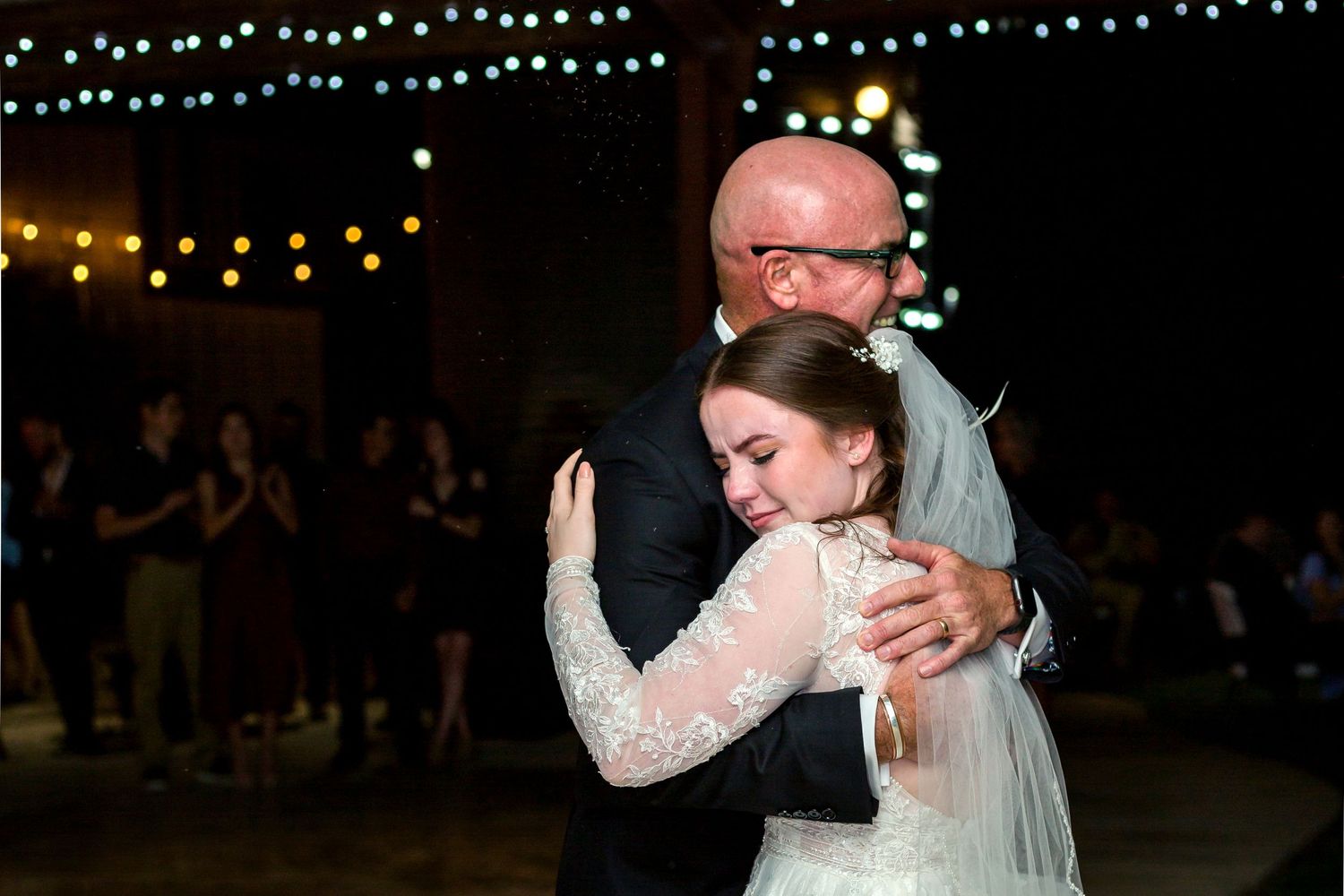 Emotional dance moment at wedding reception with string lights in background.