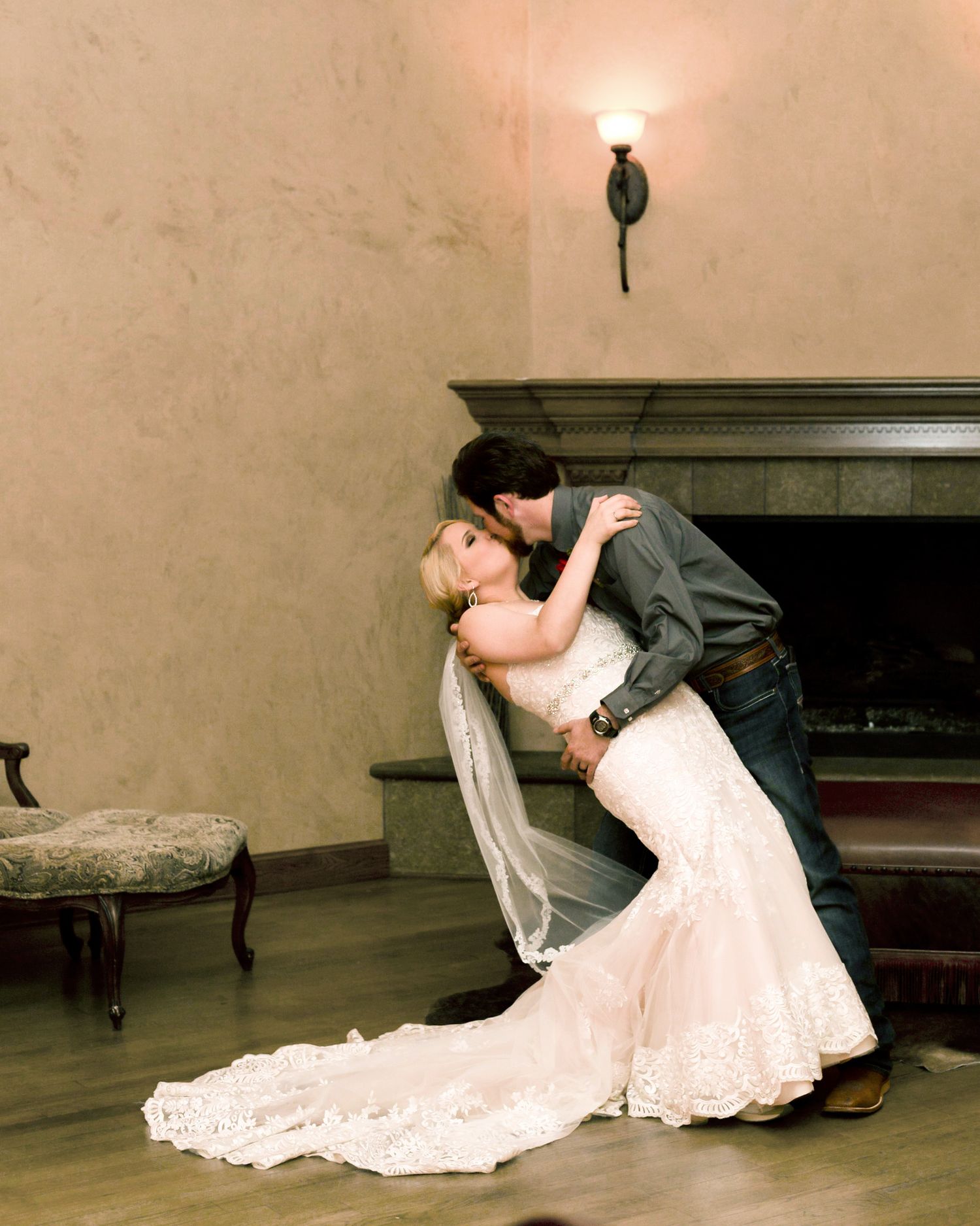 Romantic dip pose with couple in formal wear against neutral wall with sconce lighting.