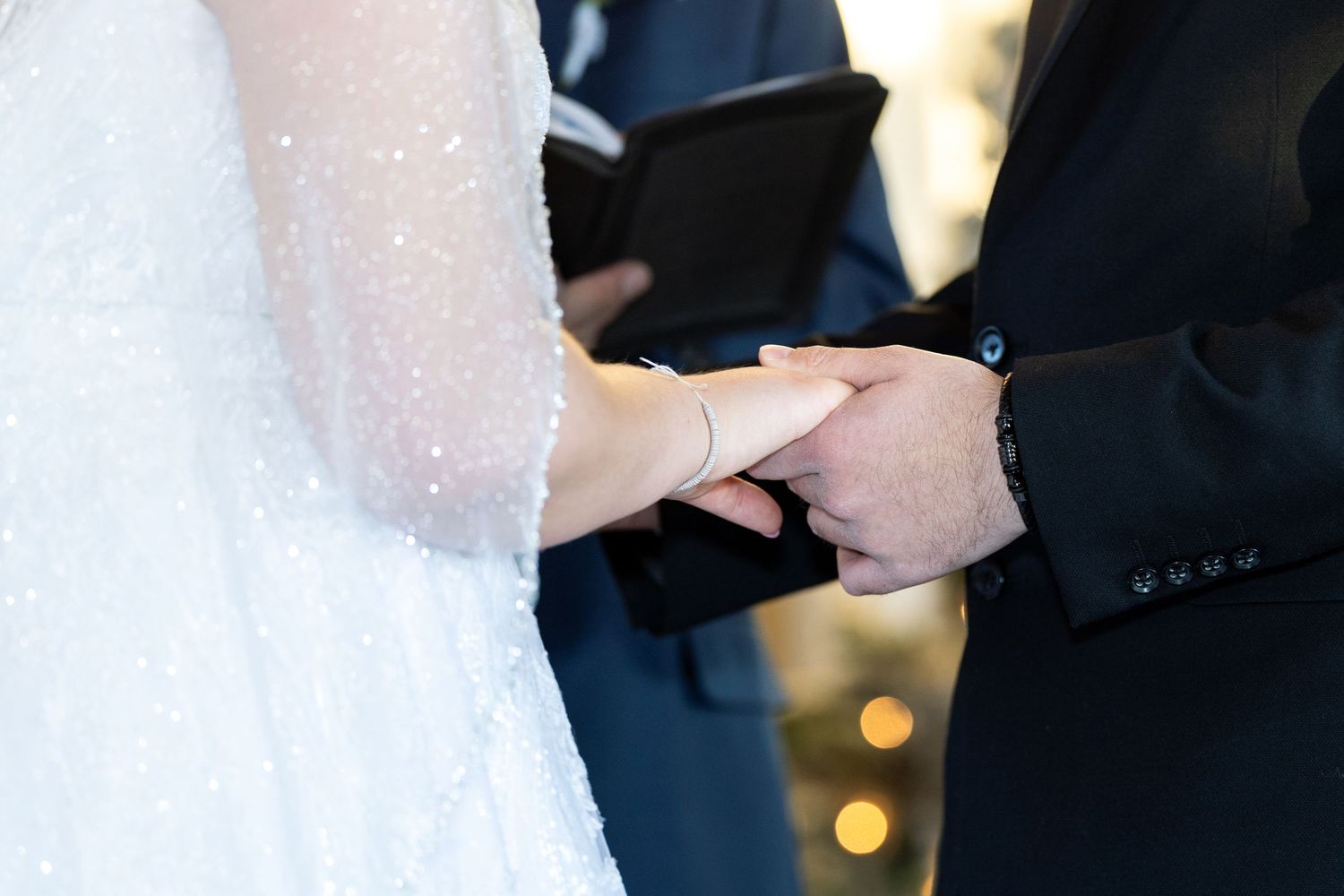 Close-up of hands exchanging wedding rings during ceremony with soft lighting.