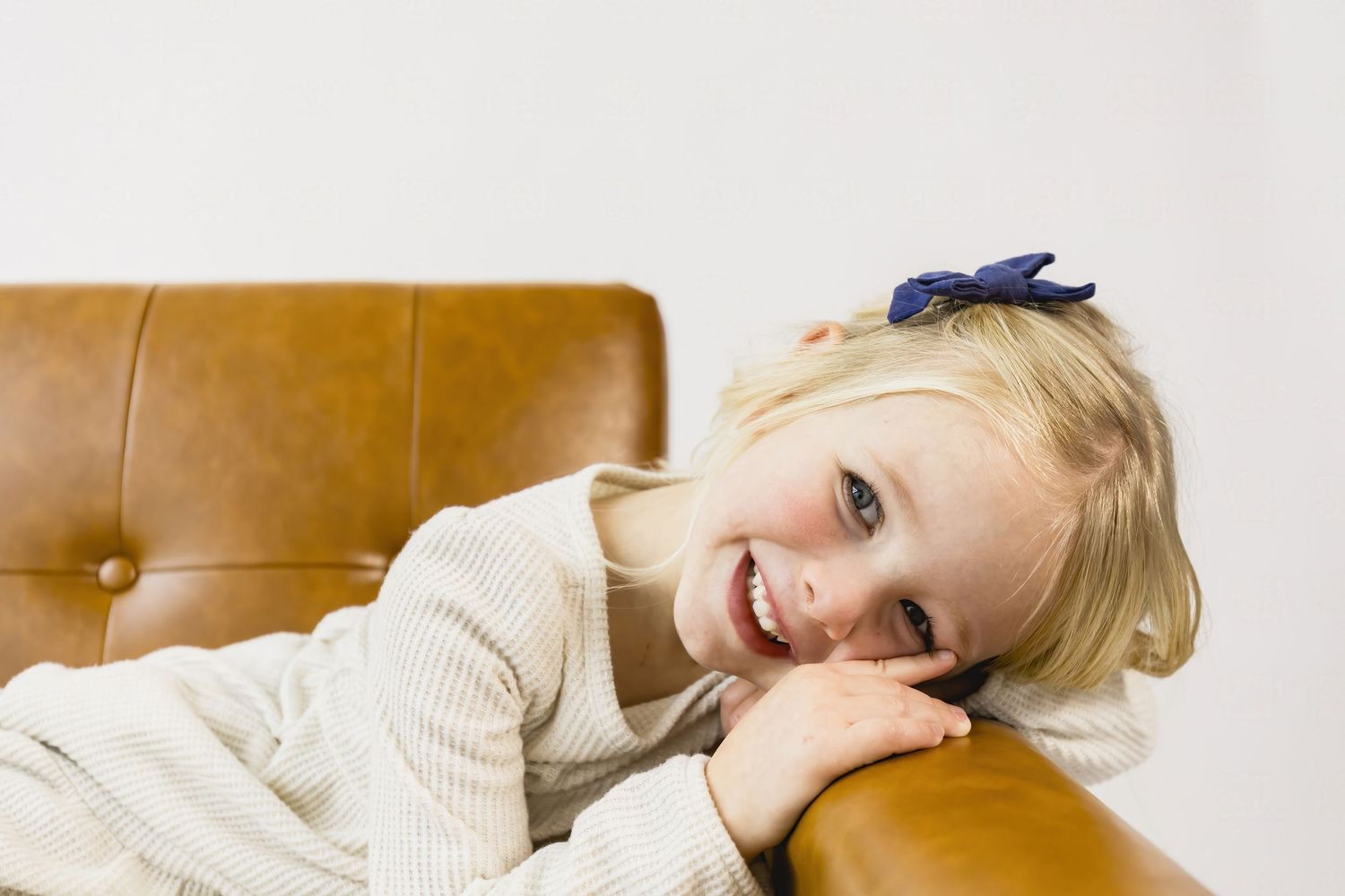 Person relaxing on a brown leather couch in a cozy white sweater.