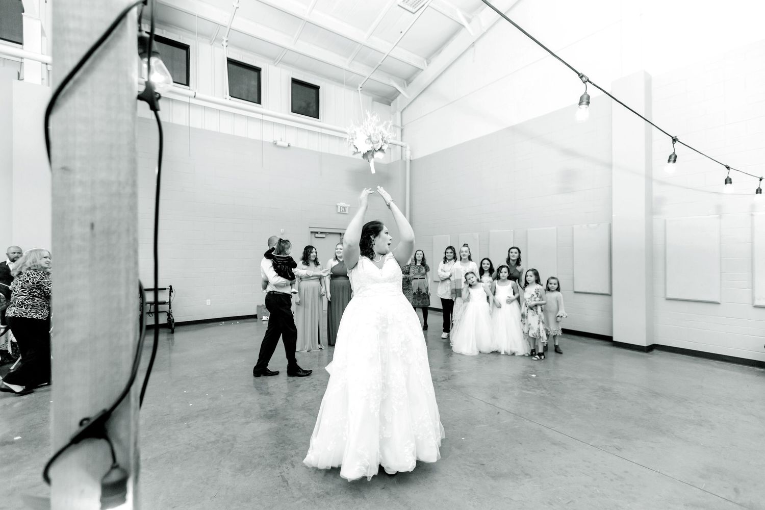 Wide angle view of an empty white wedding venue with string lights and high ceilings.