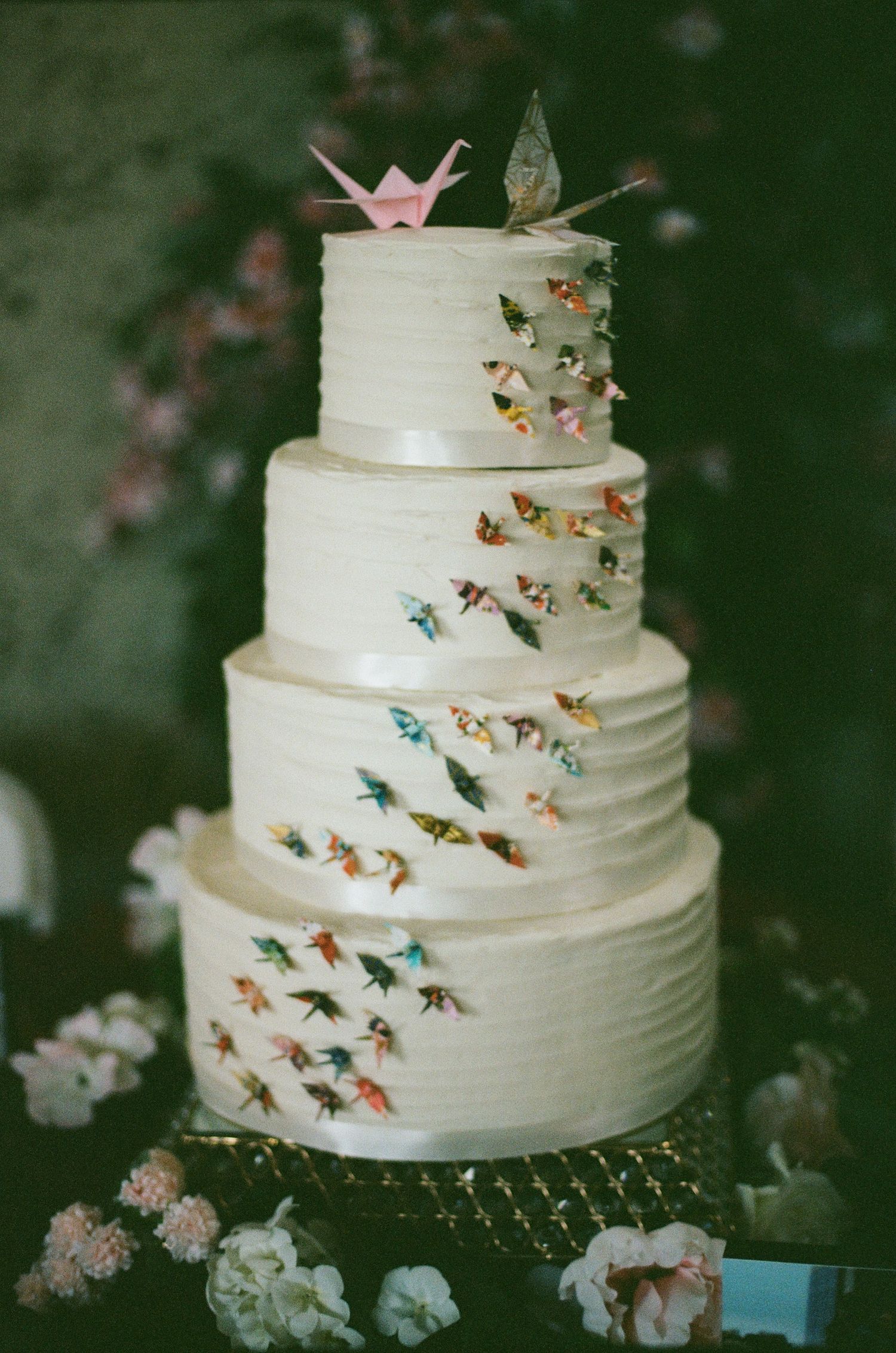 White tiered wedding cake decorated with colorful butterfly accents and crown topper.