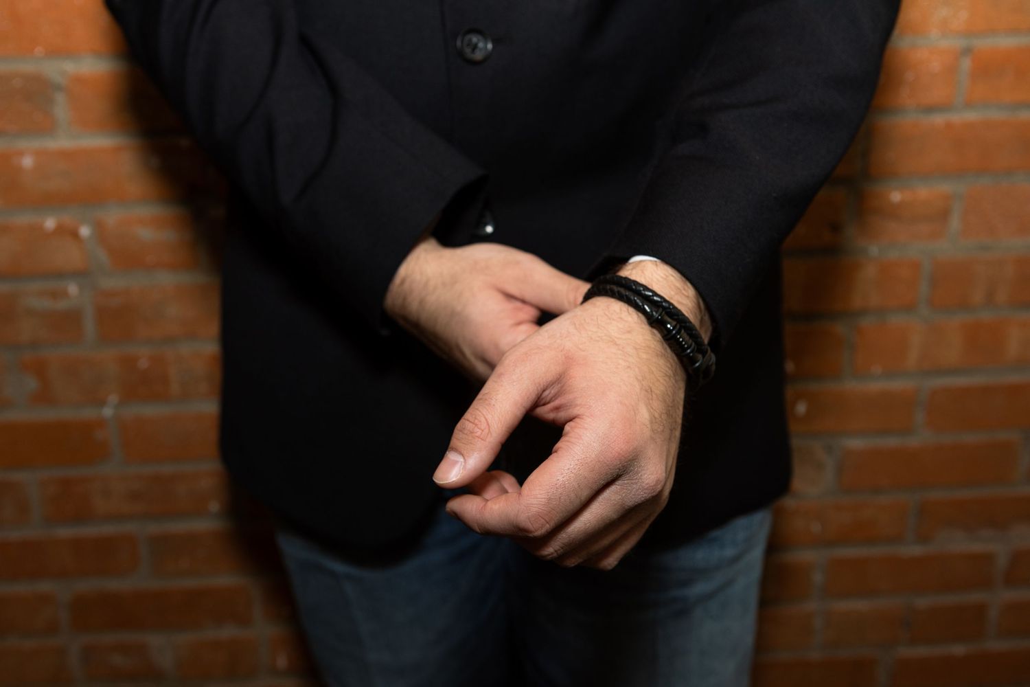Close-up of hands clasped together against a brick wall background.