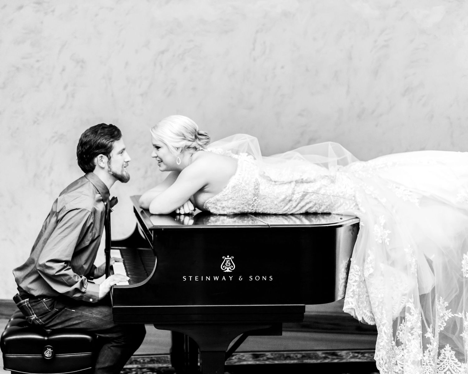Romantic black and white photo with couple posed at Steinway piano.