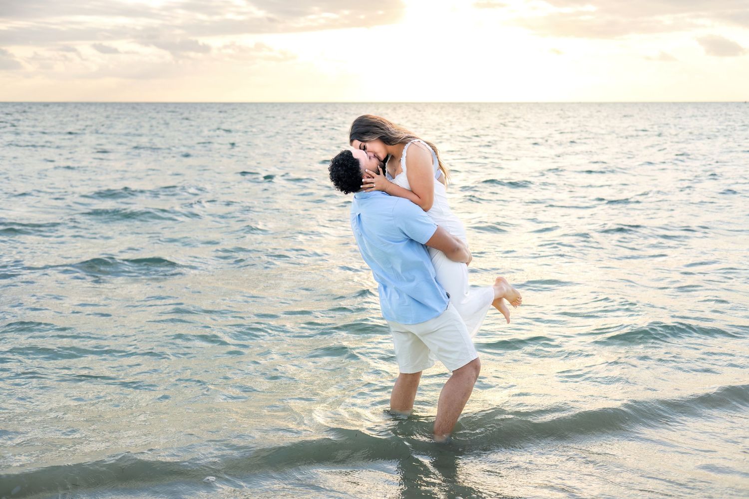 Romantic couple plays and splashes in the ocean water at sunset during a beach photoshoot.