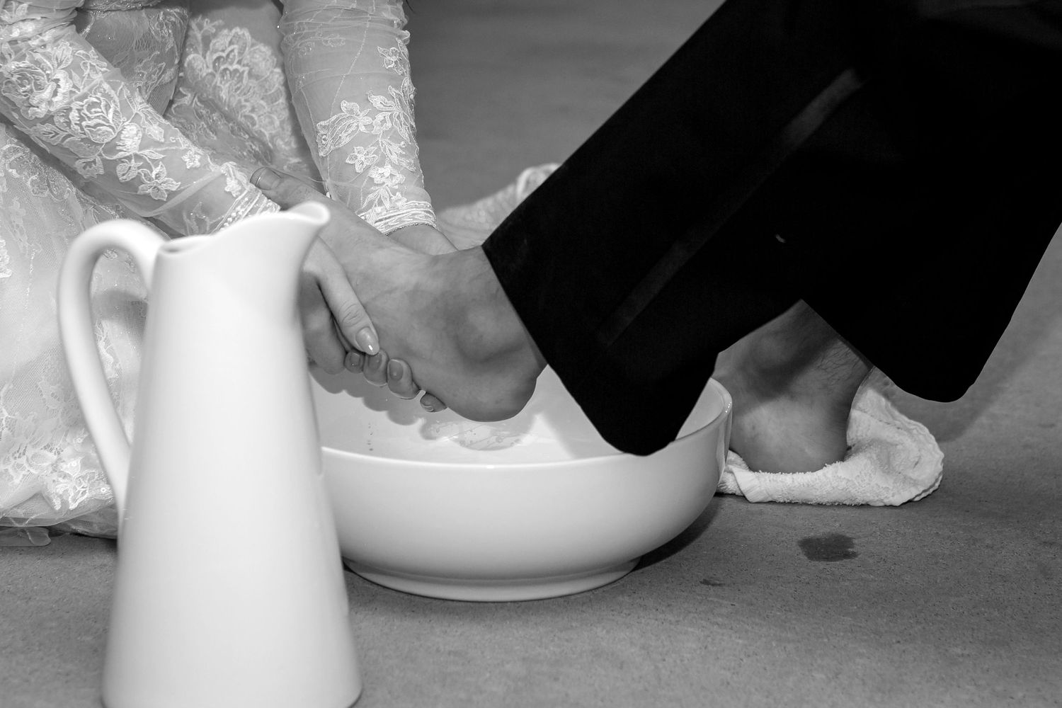Black and white photo of traditional foot washing ceremony with white basin and pitcher.