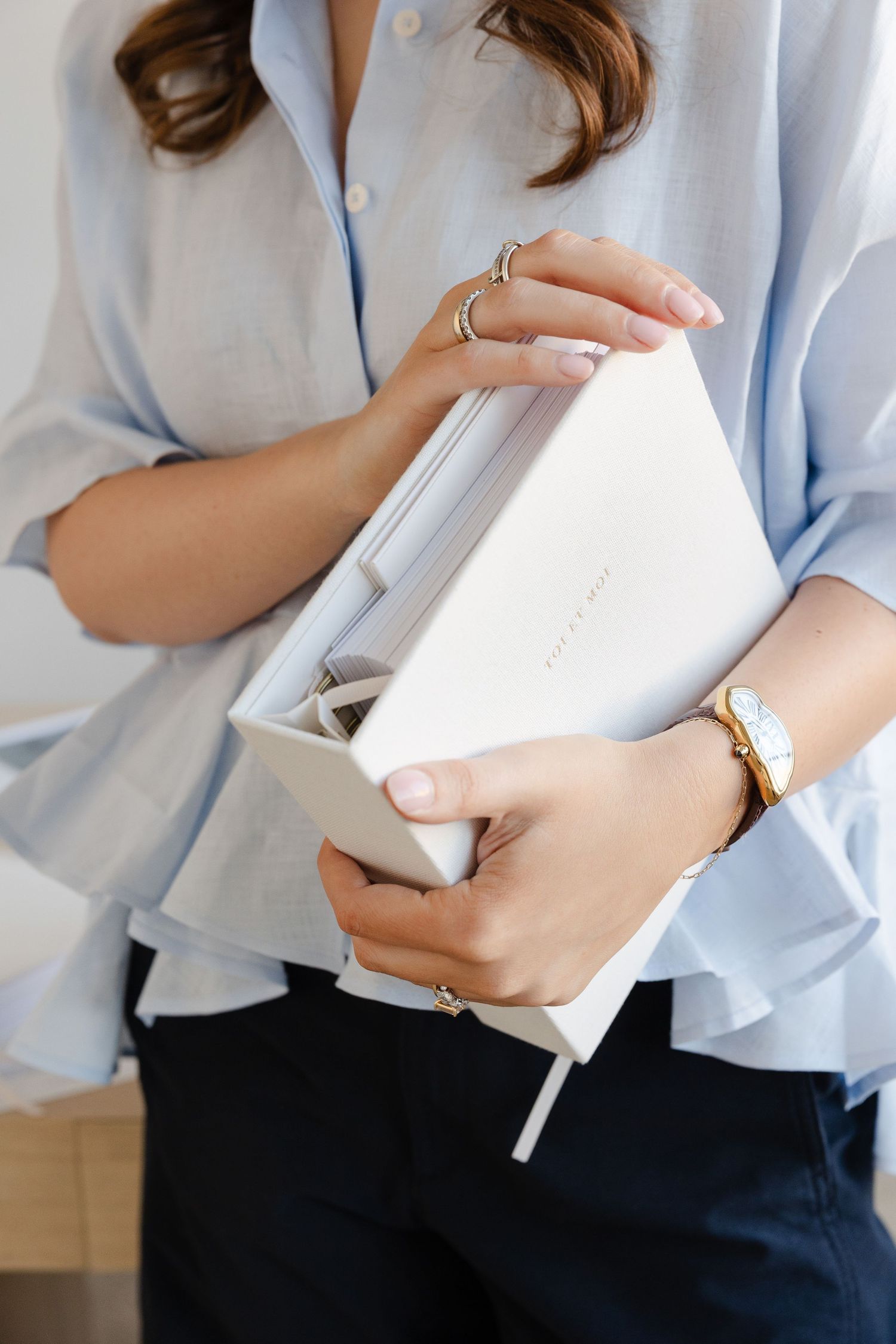 Person in light blue shirt holding white paper materials while standing.