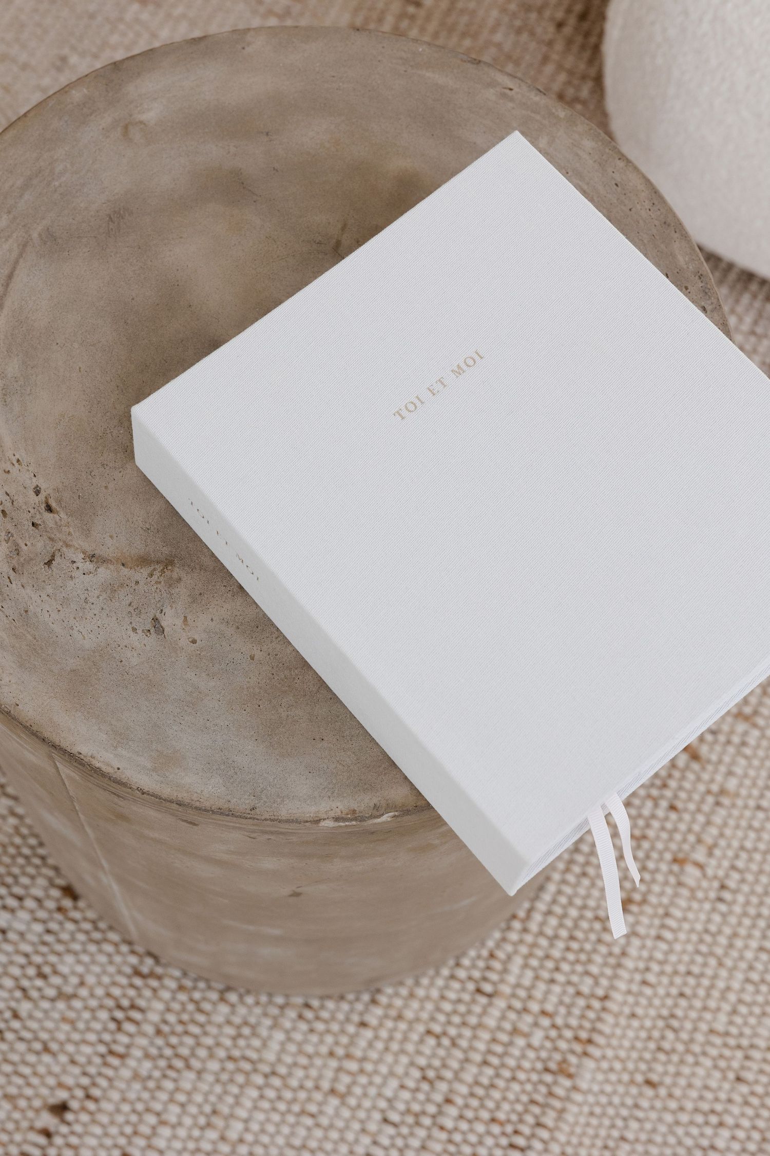 Minimalist white notebook or card displayed on textured beige surface.