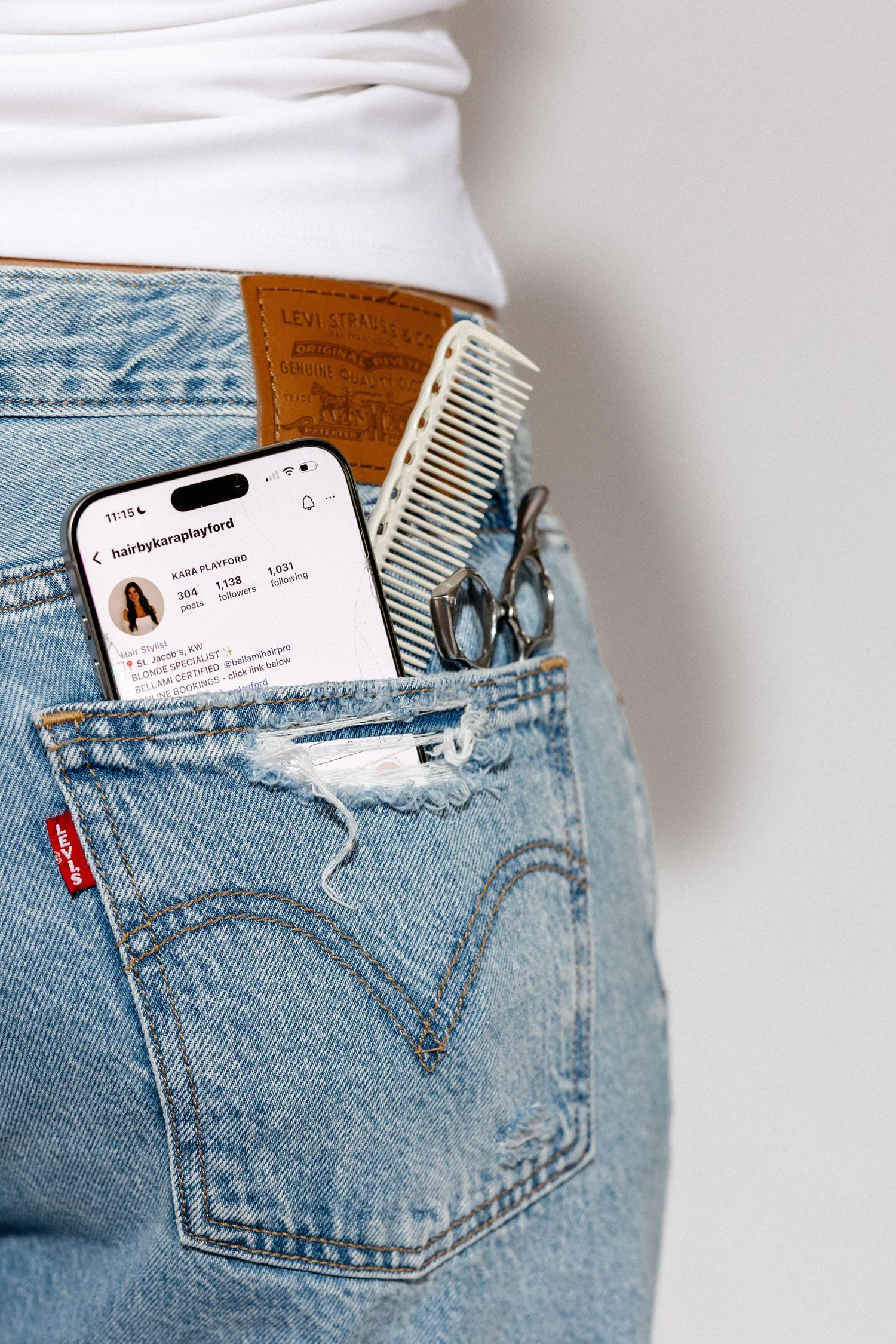 Light wash denim jeans pocket with a white smartphone and comb peeking out.