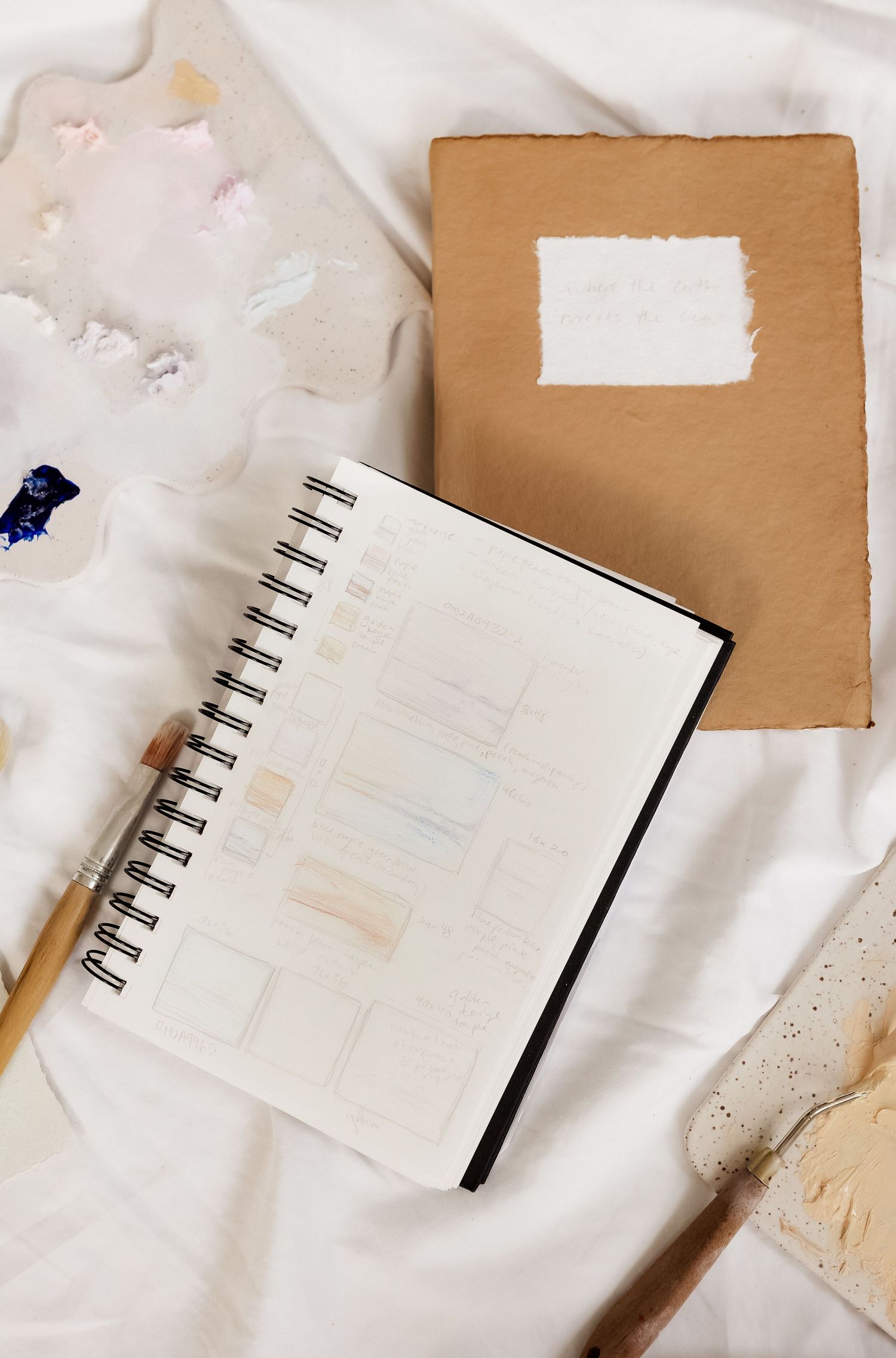 Spiral notebook with brown cover and art supplies arranged on white surface.