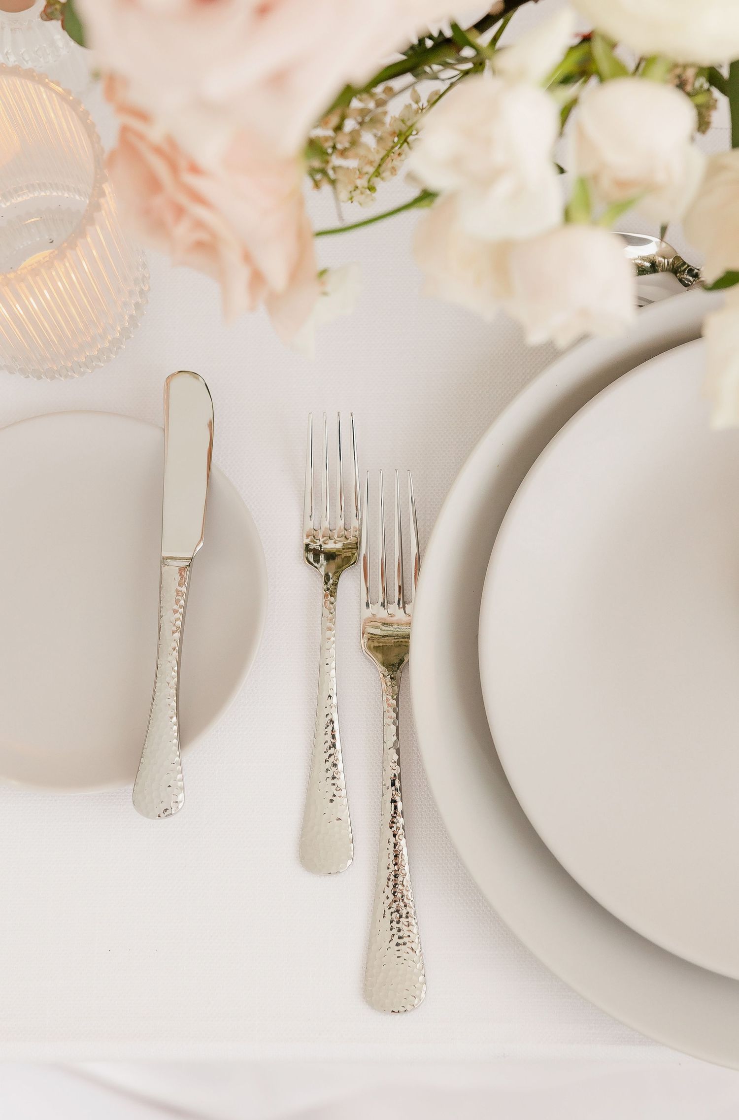 Vintage silverware and white plates arranged on a light tablecloth with elegant details.
