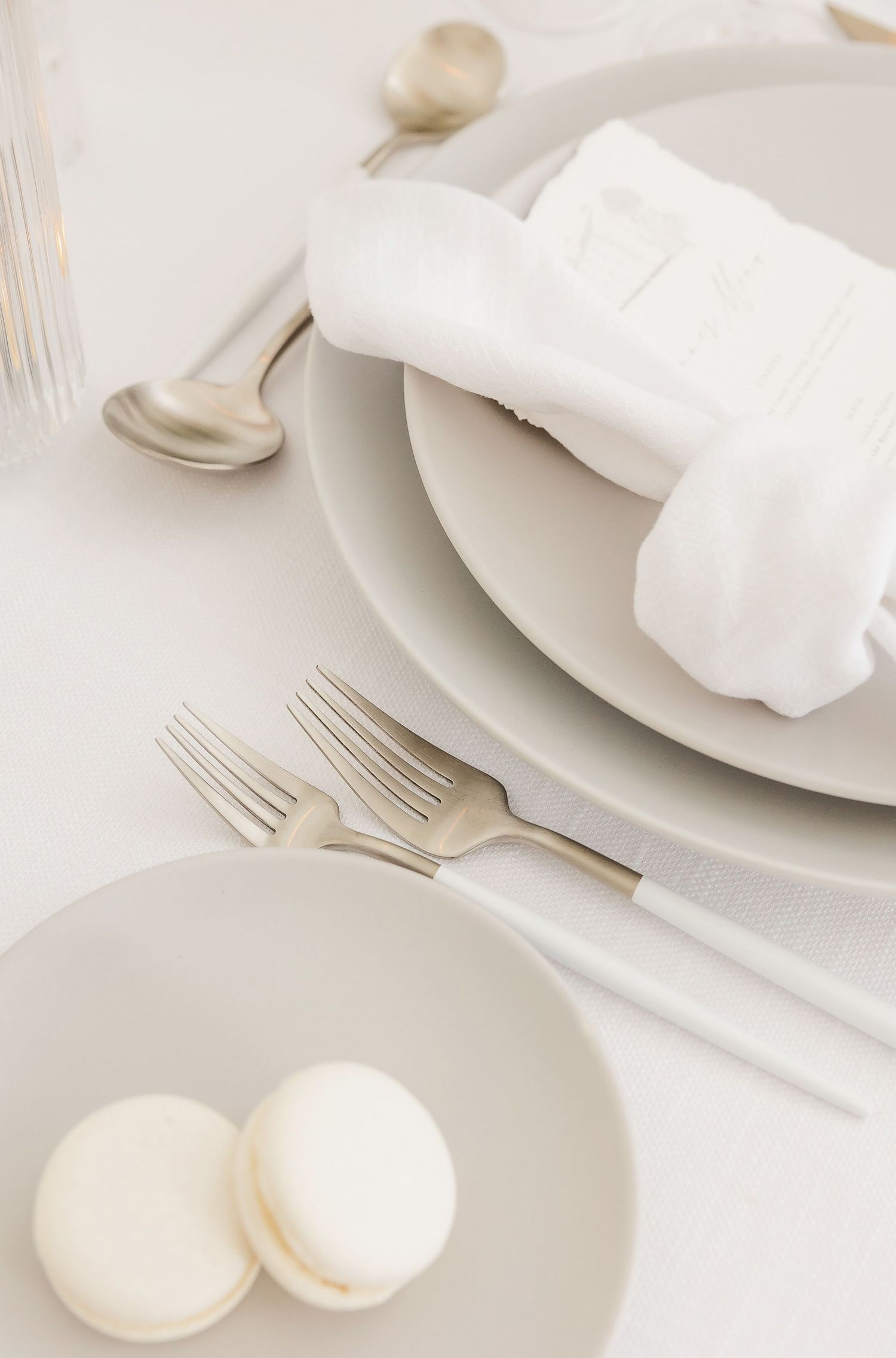 Minimalist white place setting with folded napkin and macarons on porcelain plates.