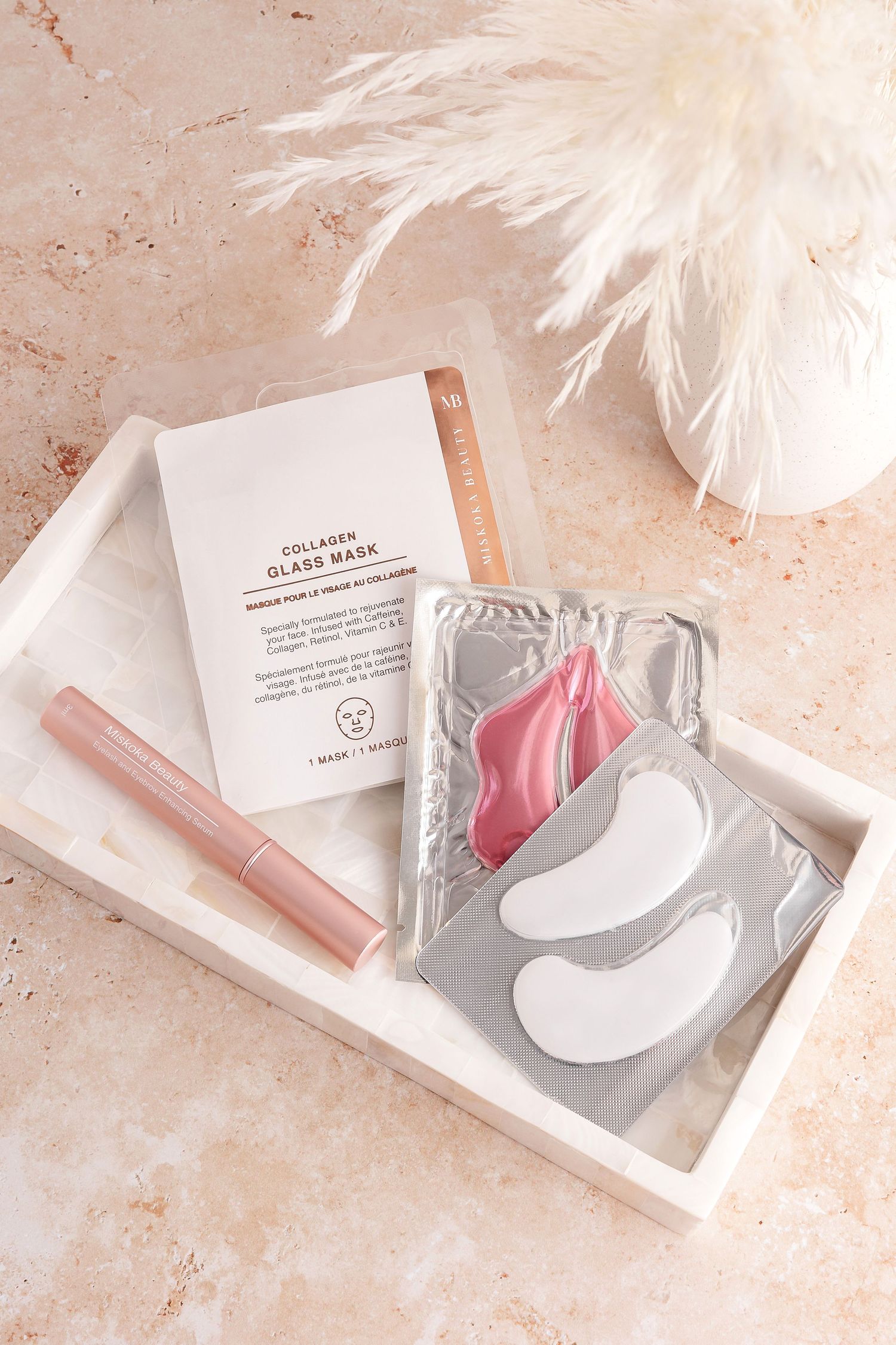 Pink under-eye patches displayed with skincare packaging on beige marble surface.