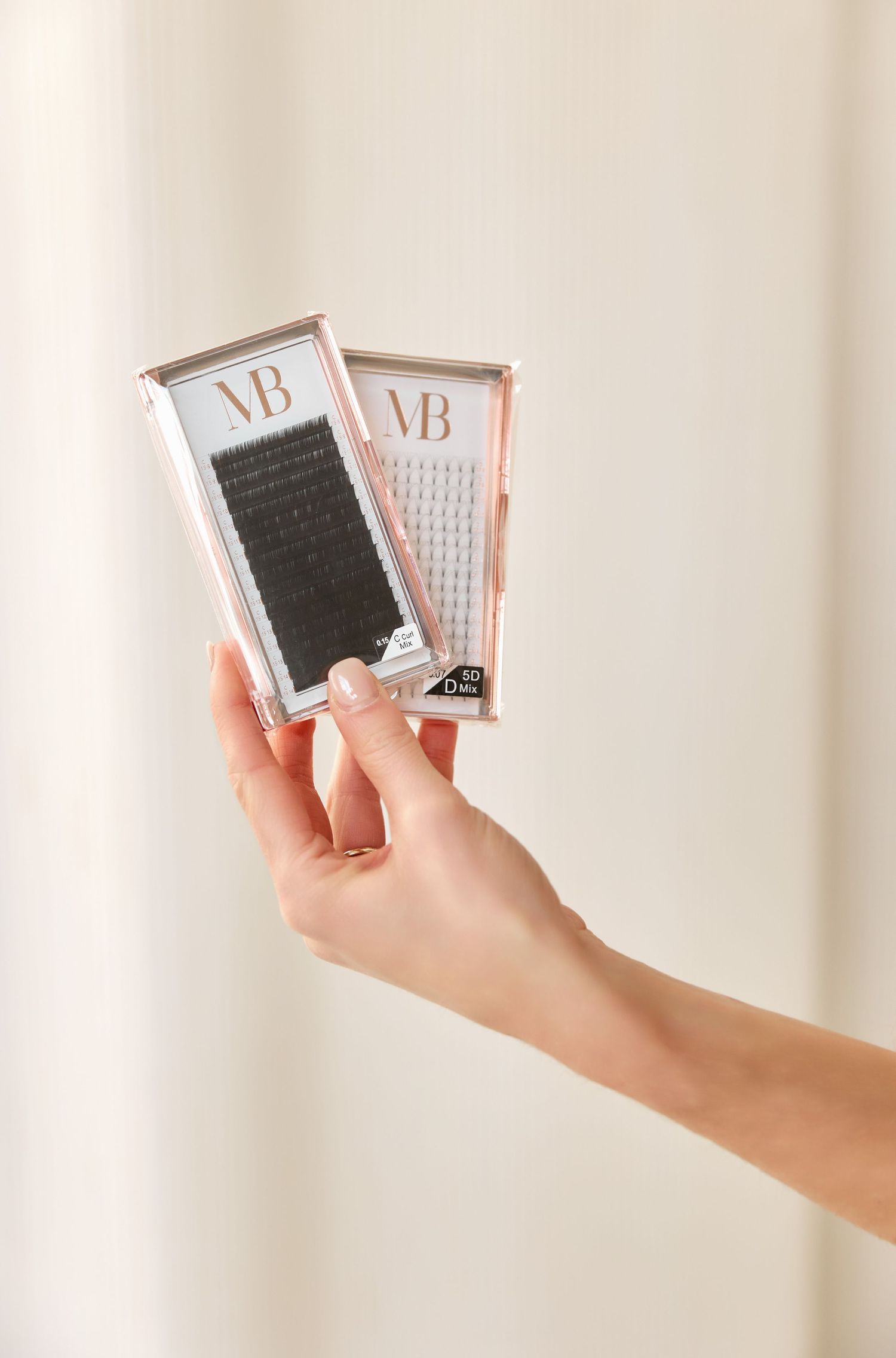 Hands holding multiple eyelash extension trays displaying different lash styles against a light background.