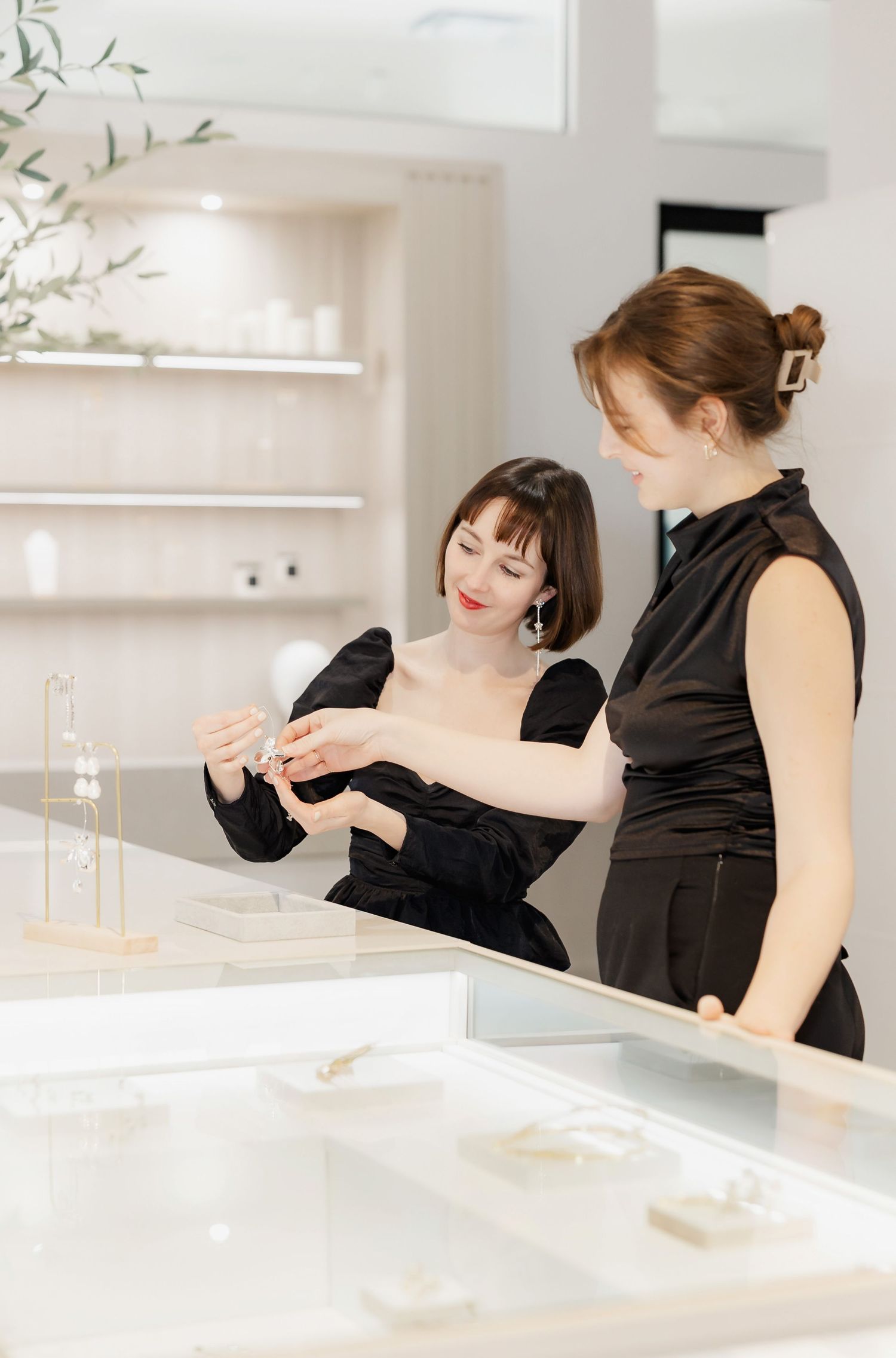 Customers browse jewelry items at an elegant white retail counter display.