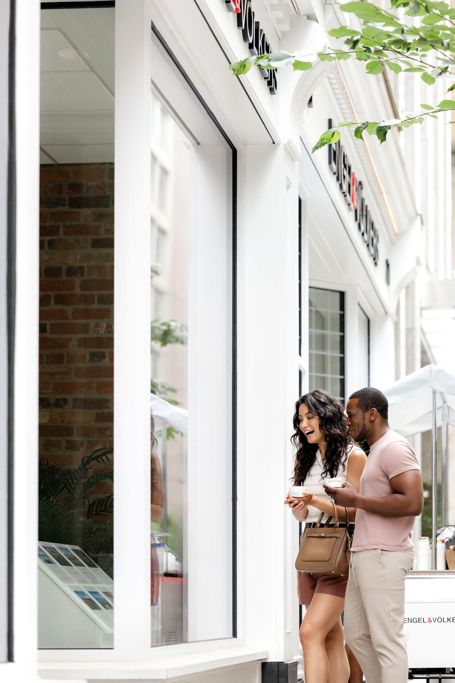 Couple looking at property listings outside a modern real estate office.