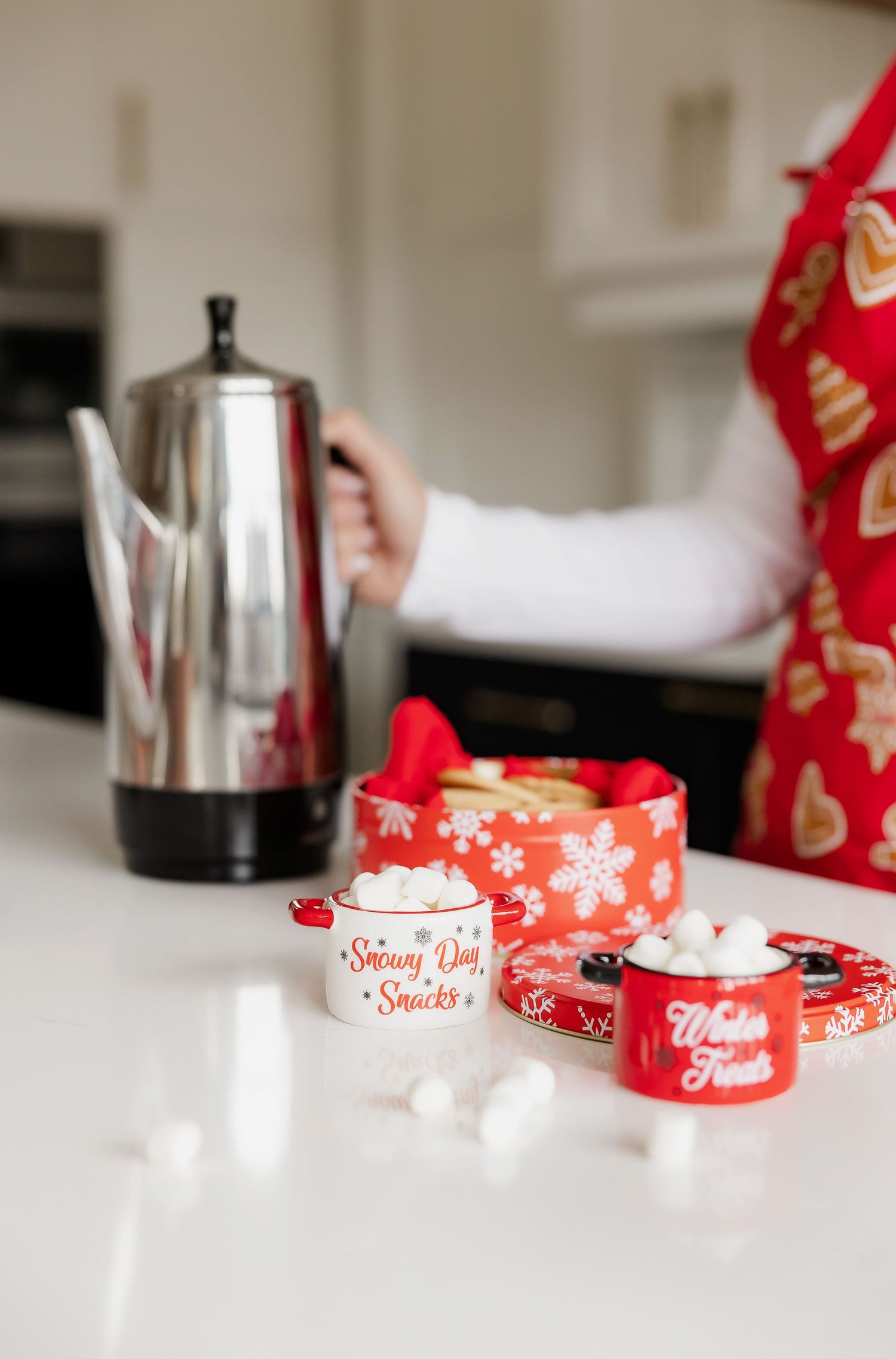 Holiday themed coffee setup with red decorative tins and silver coffee pot on white counter.