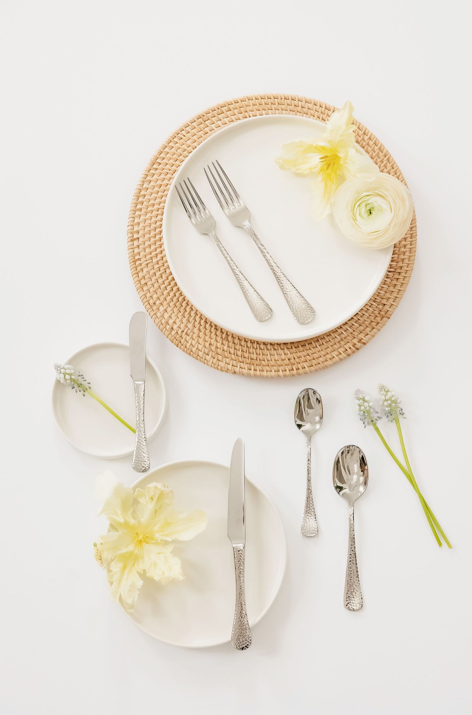 White place settings with silver cutlery and yellow flowers on woven placemats.