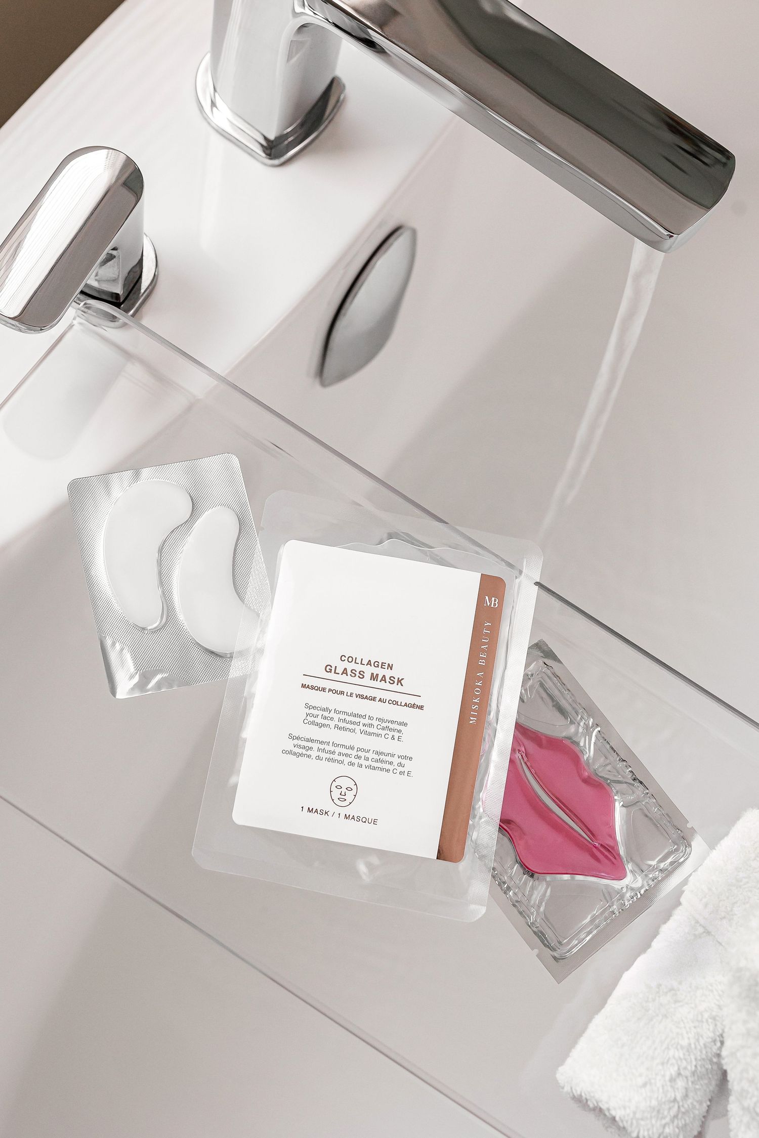 White bathroom counter with beauty product packaging and toiletries reflected in mirror.