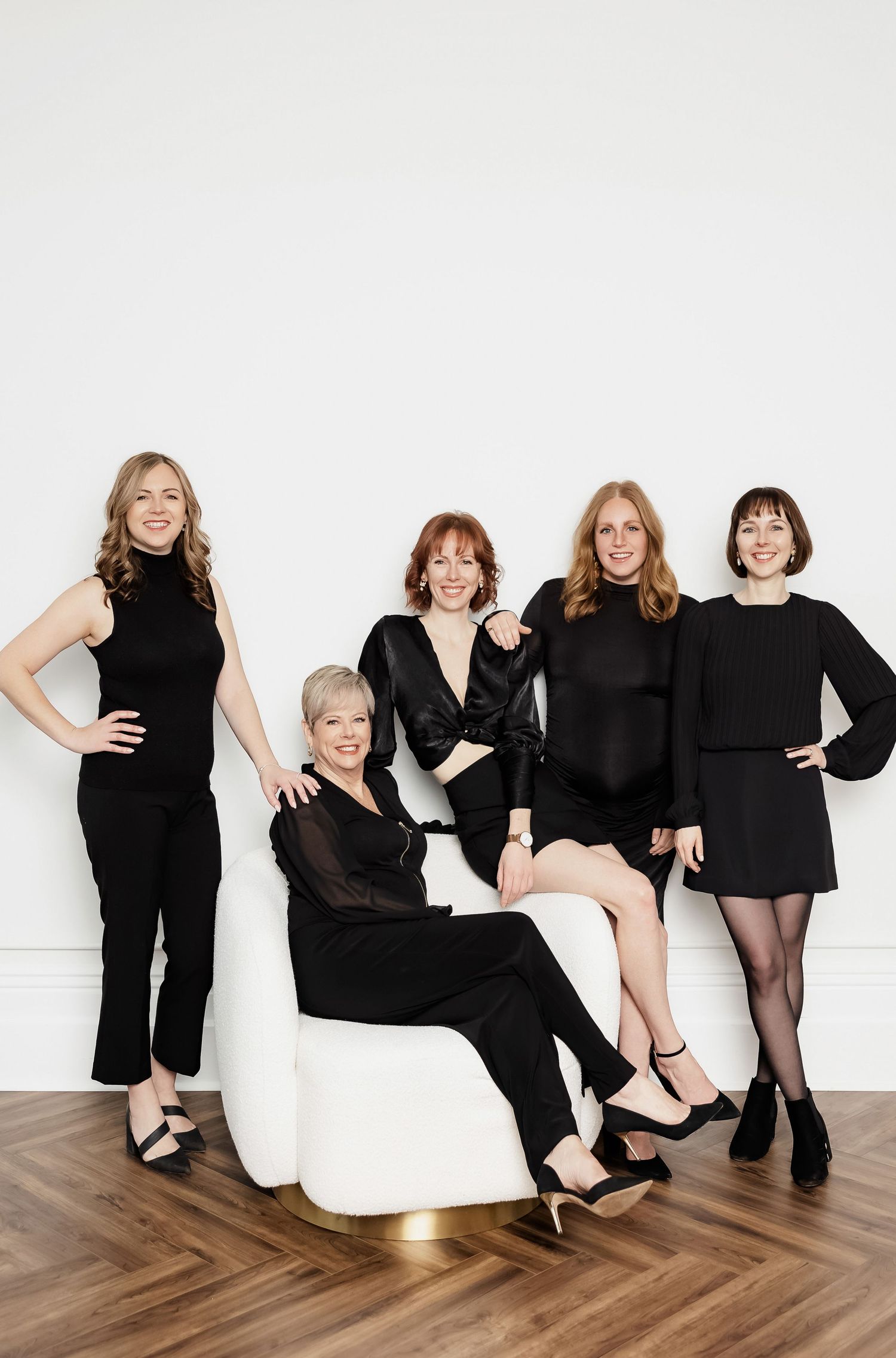Models in black attire pose playfully together around white bean bag chair.