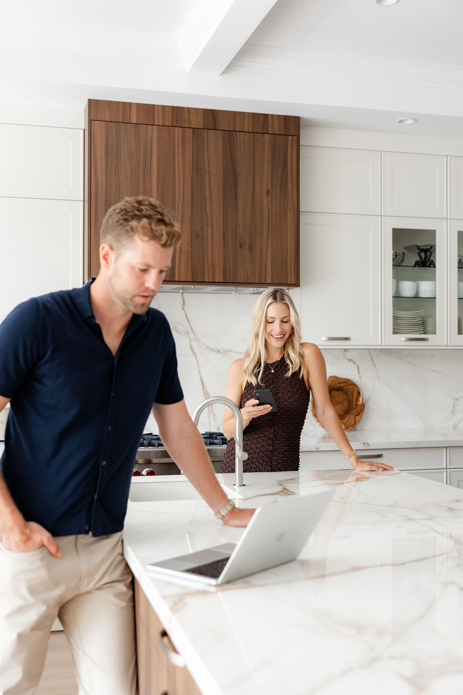Two people collaborate while working on a laptop in a modern white kitchen.