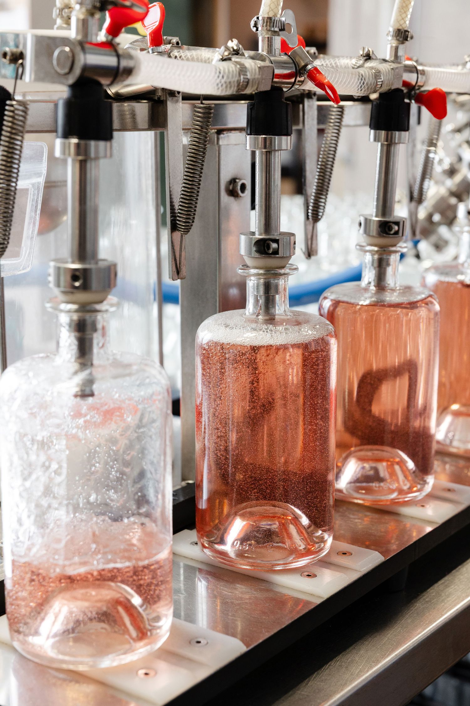 Glass bottles of pink wine being filled on an automated bottling line.