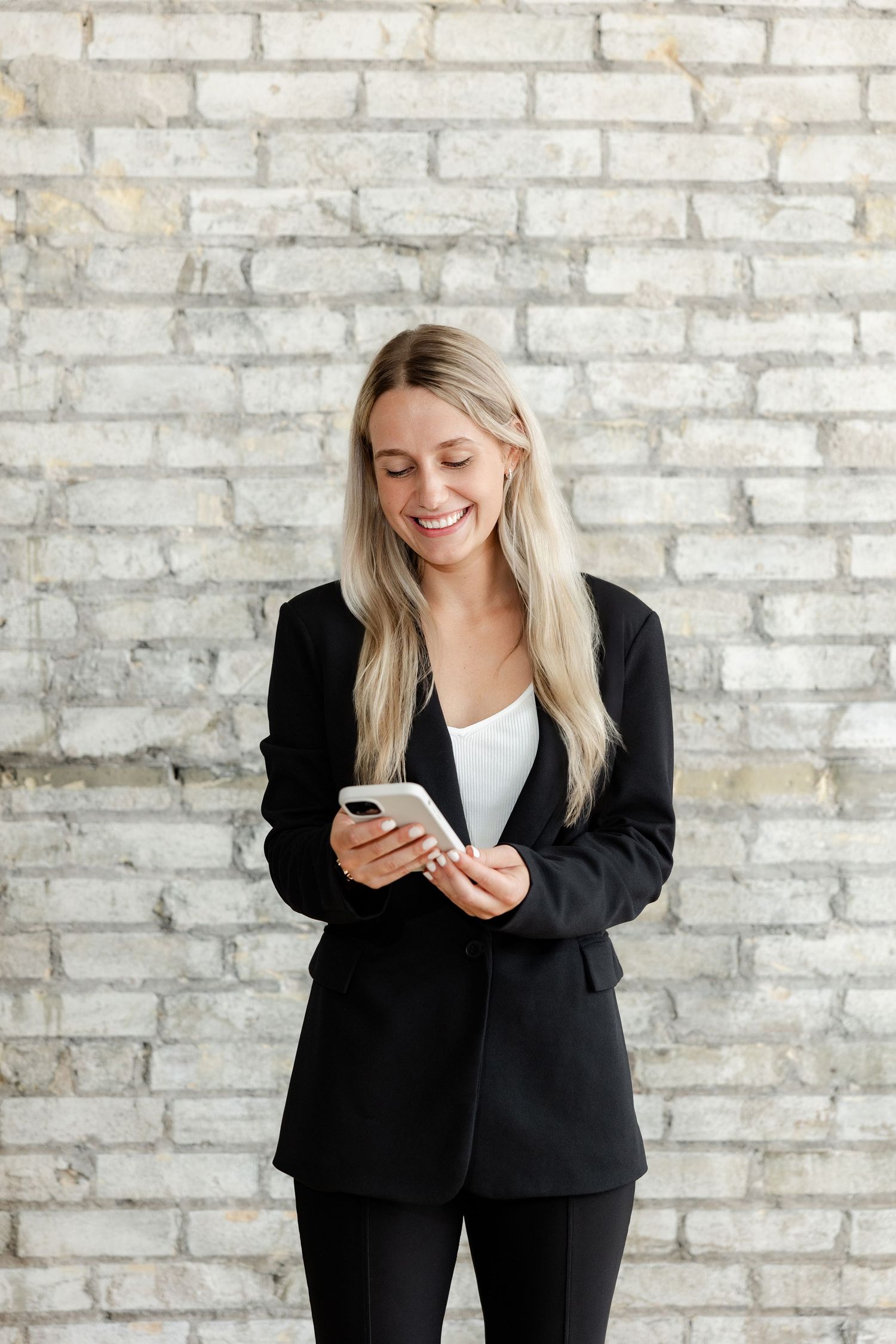 Professional checking smartphone against white brick wall background.