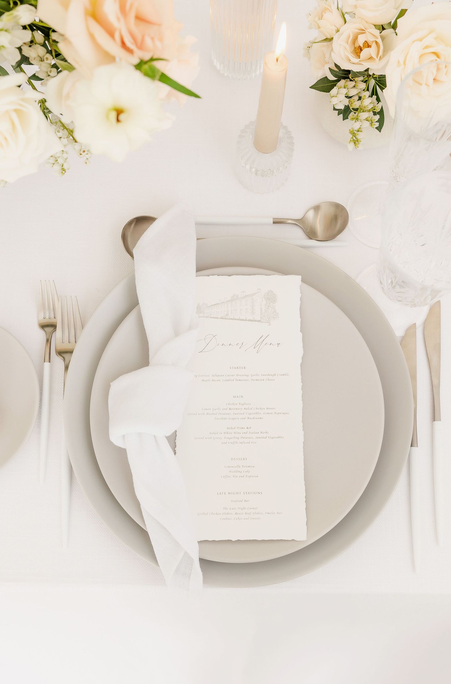 Romantic place setting with soft pink roses and white menu cards on light gray dinnerware.