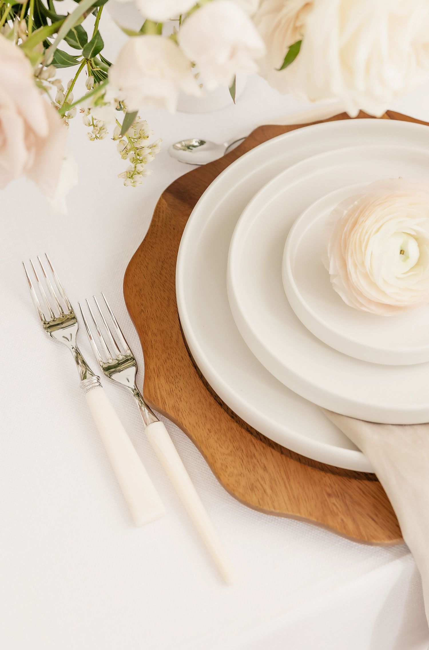 Elegant white place setting on wooden charger with vintage silverware and floral accents.